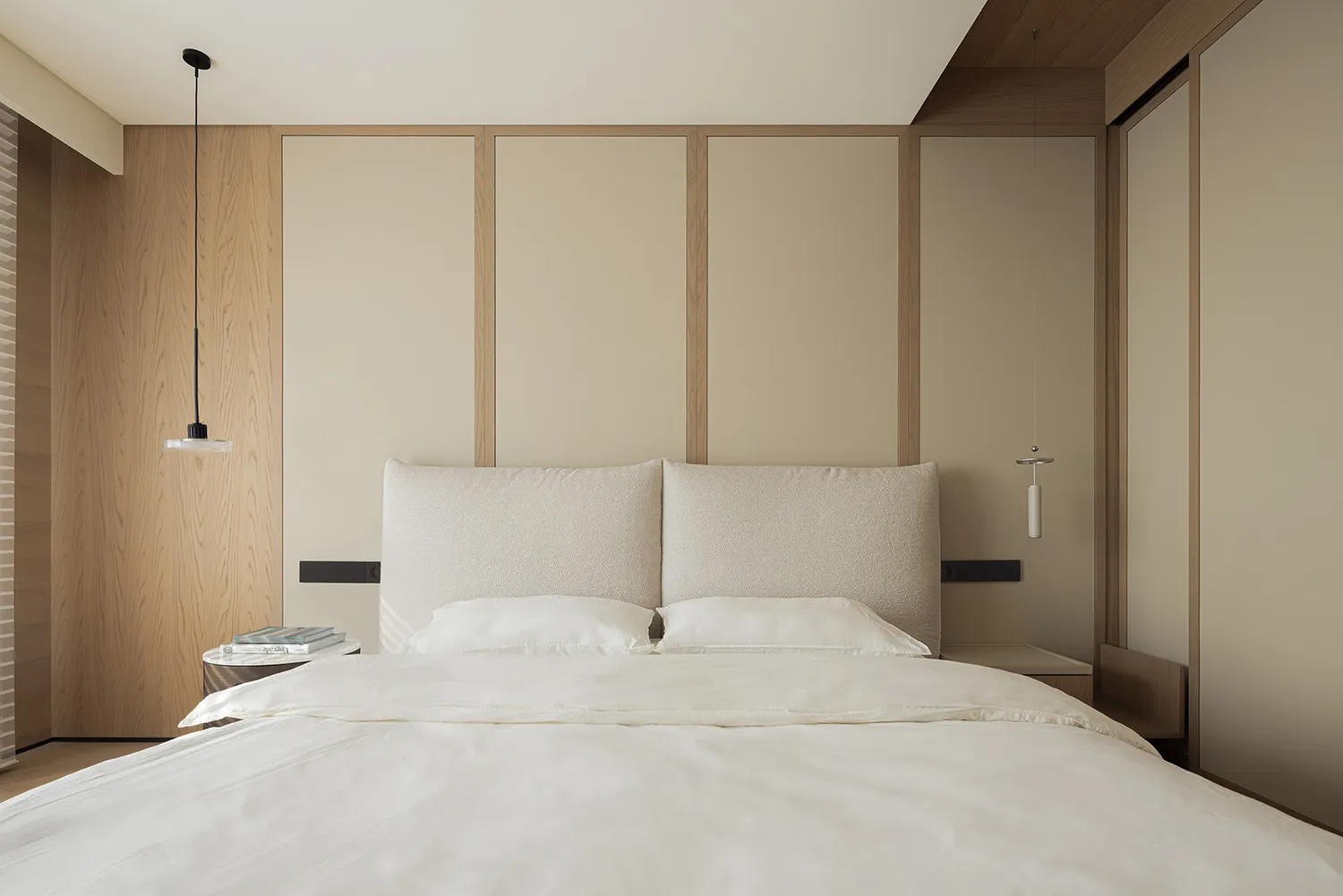 Modern minimalist bedroom featuring a large bed with a textured beige fabric headboard, white bedding, light oak wood paneling on the wall, and matching floating nightstands with pendant lights.