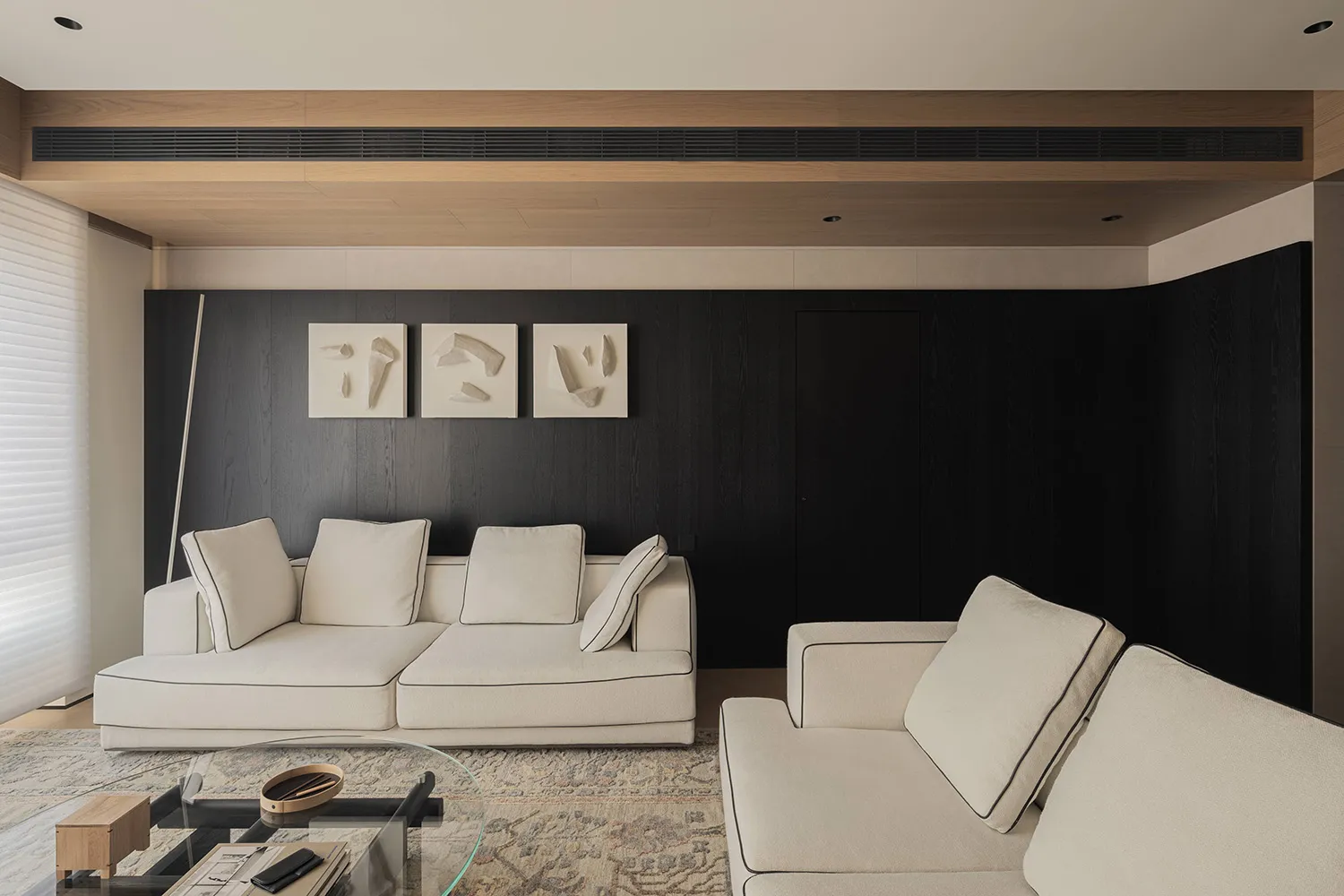 Modern living room featuring a dark wood accent wall, white L-shaped sectional sofa, glass coffee table on a patterned area rug, and three abstract wall sculptures.