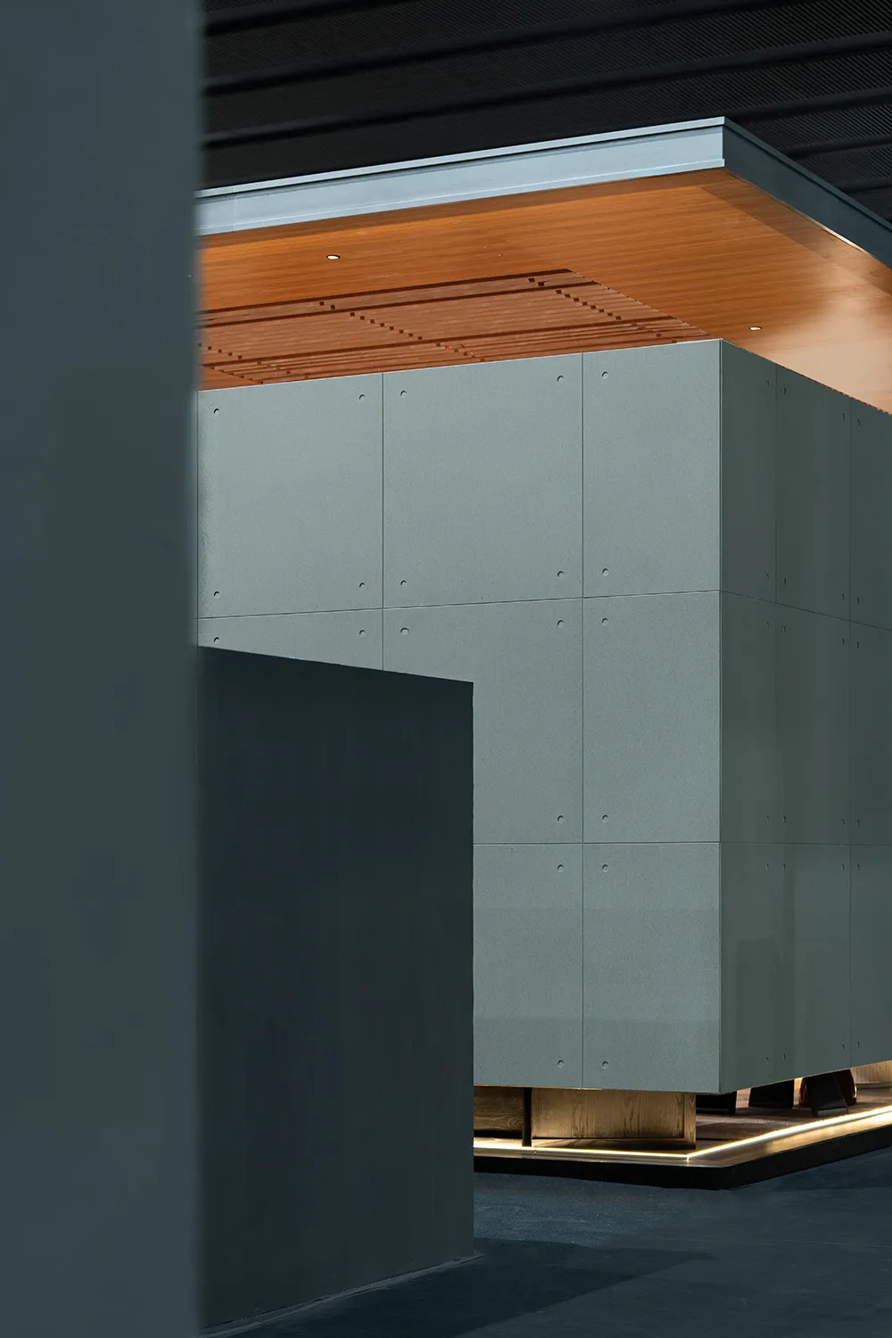現代建築室內，懸浮清水模大型櫃體展露螺栓細節，搭配溫潤木質線條天花板與底部間接照明。