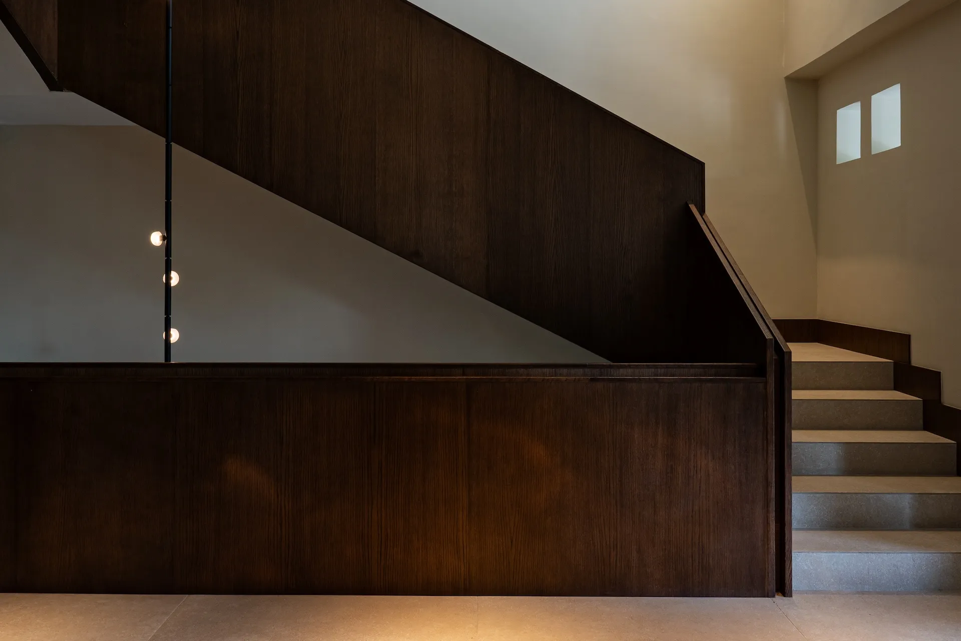 Modern minimalist interior featuring a dark walnut wood staircase with vertical pendant lighting and concrete steps.