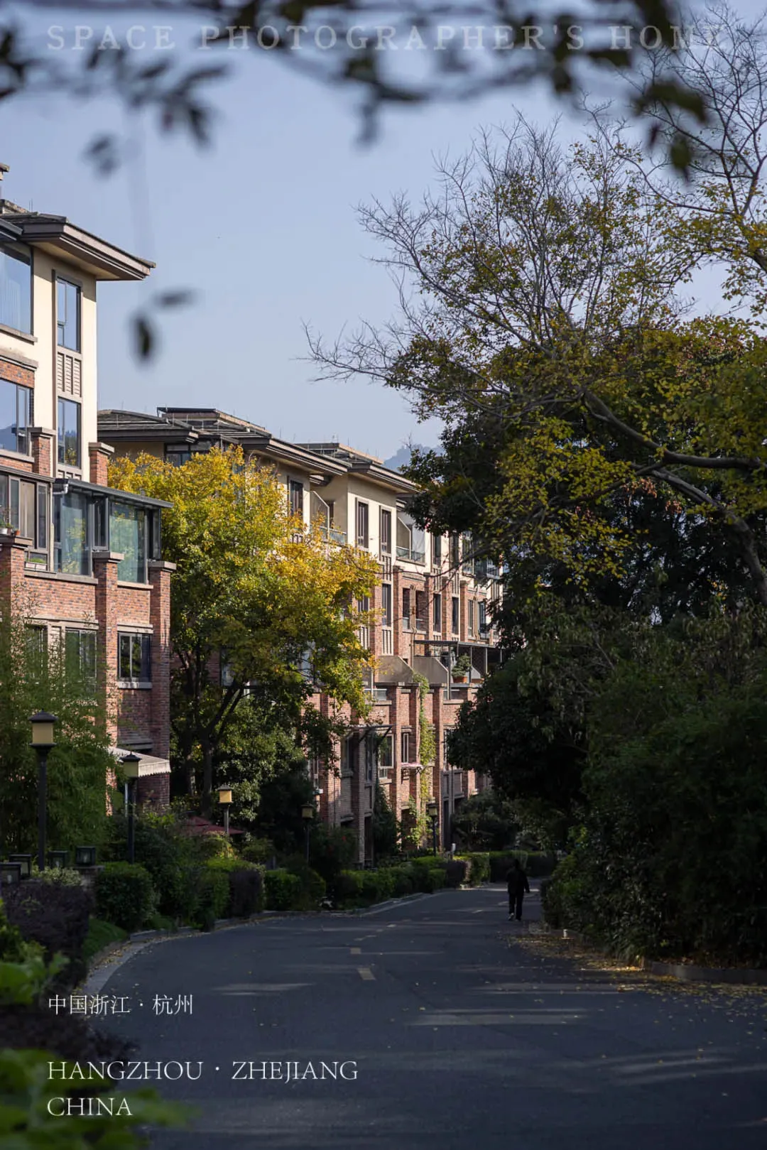 Tree-lined pathway through a modern residential community featuring brick and stucco townhouses in Hangzhou, Zhejiang, China during autumn.