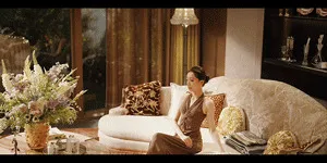 Woman in a beige dress relaxing on a curved cream boucle sofa beside a large floral arrangement in an elegant living room
