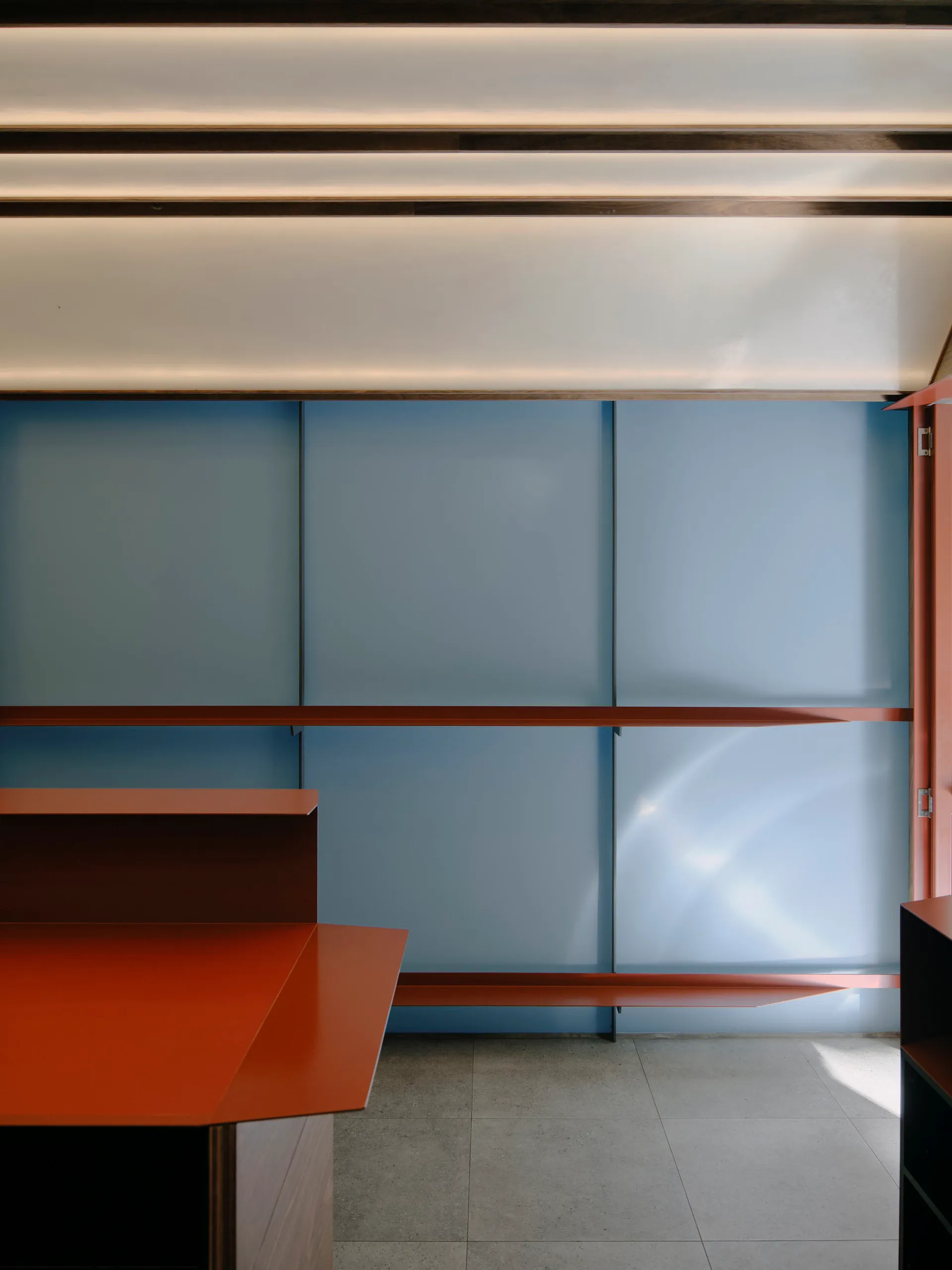 Modern interior featuring a terracotta-colored storage unit and large blue cabinet doors with integrated lighting and concrete flooring