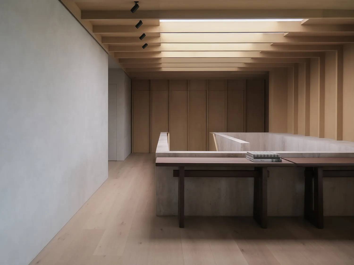 Modern minimalist interior featuring a concrete reading nook with a dark oak bench and stacked books, under a sculptural wooden ceiling with recessed lighting.