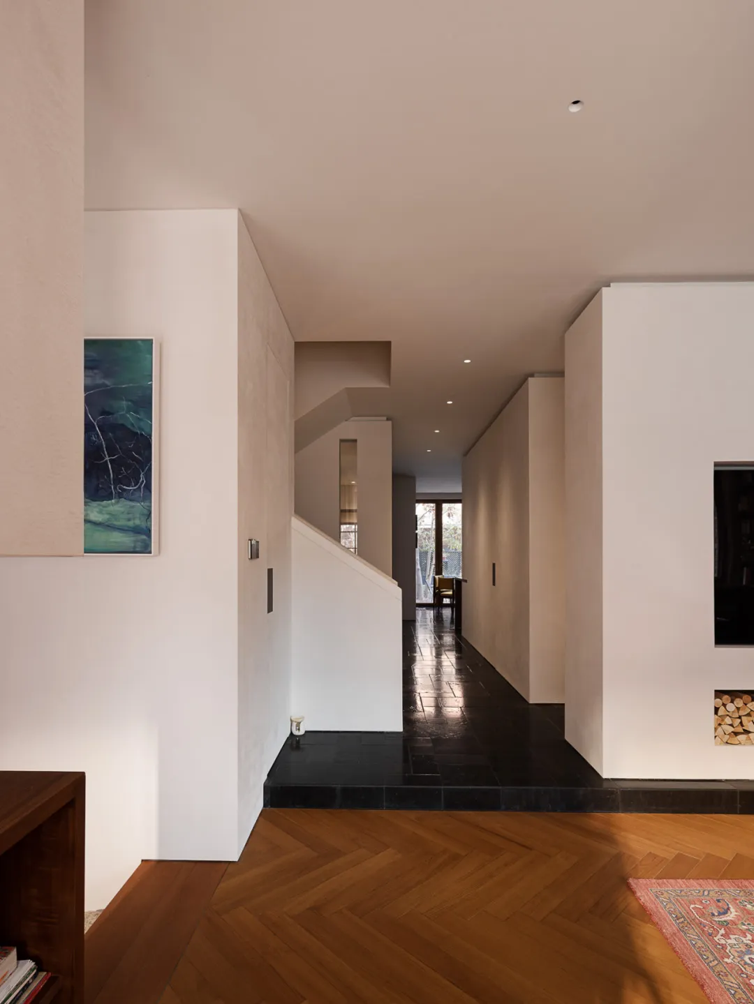 Modern minimalist interior hallway featuring herringbone pattern oak wood flooring, black slate tile entry, white textured walls, and a staircase with integrated storage.