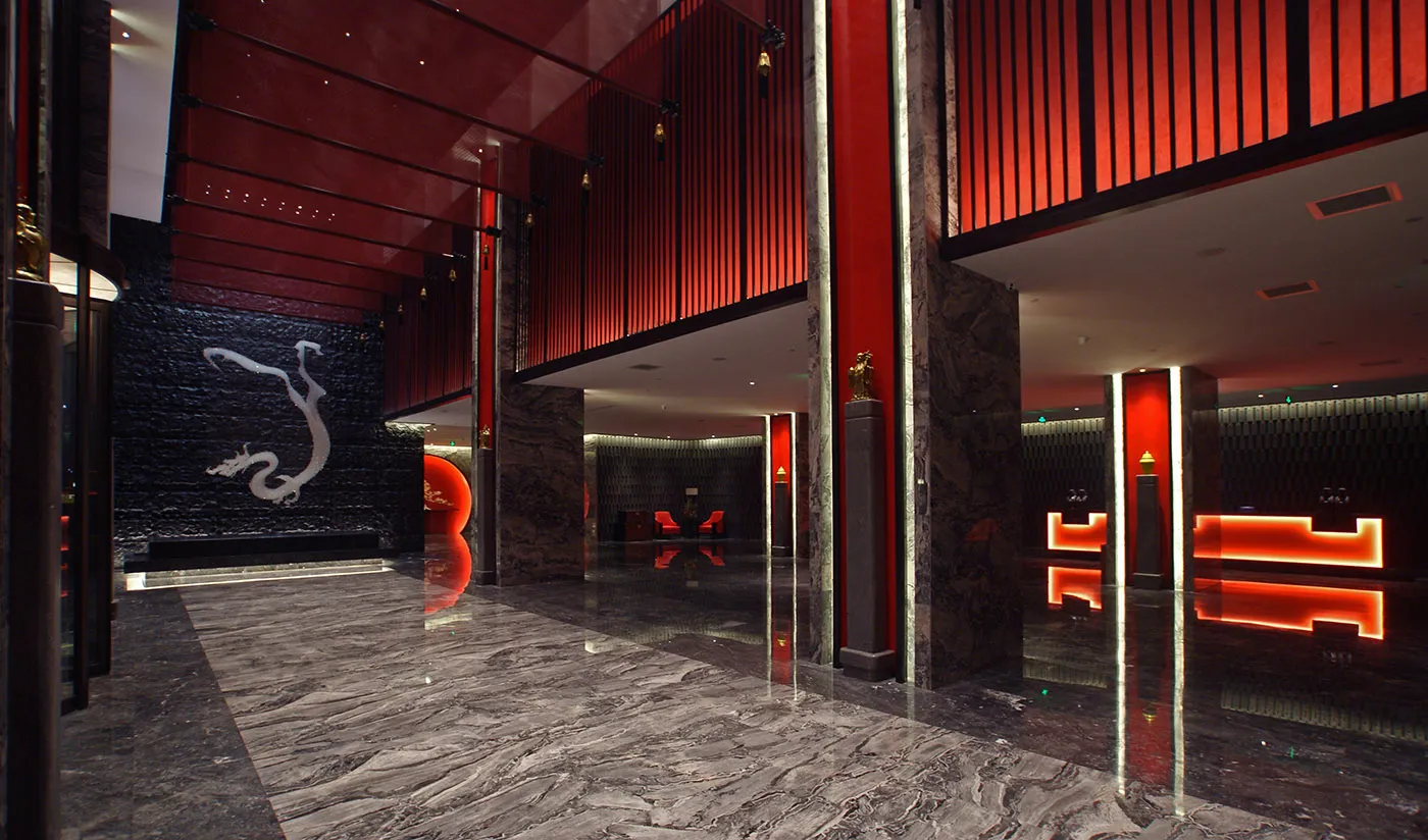 Luxurious hotel lobby featuring polished grey marble floors, dramatic red lacquered walls, a black stone dragon relief wall, and glowing red neon light installations.