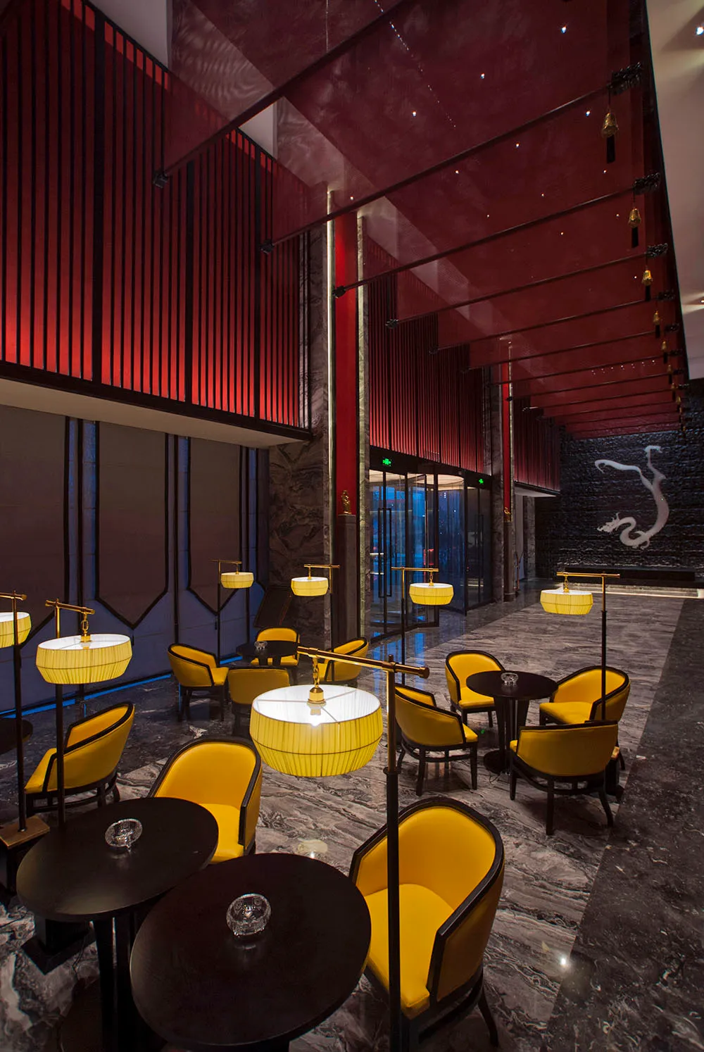 奢華飯店大廳休憩區,設有鮮黃色絨布扶手椅、黑色圓桌、戲劇感的紅色垂直板條牆,以及灰色大理石地板,背景有大型白色龍形壁畫。