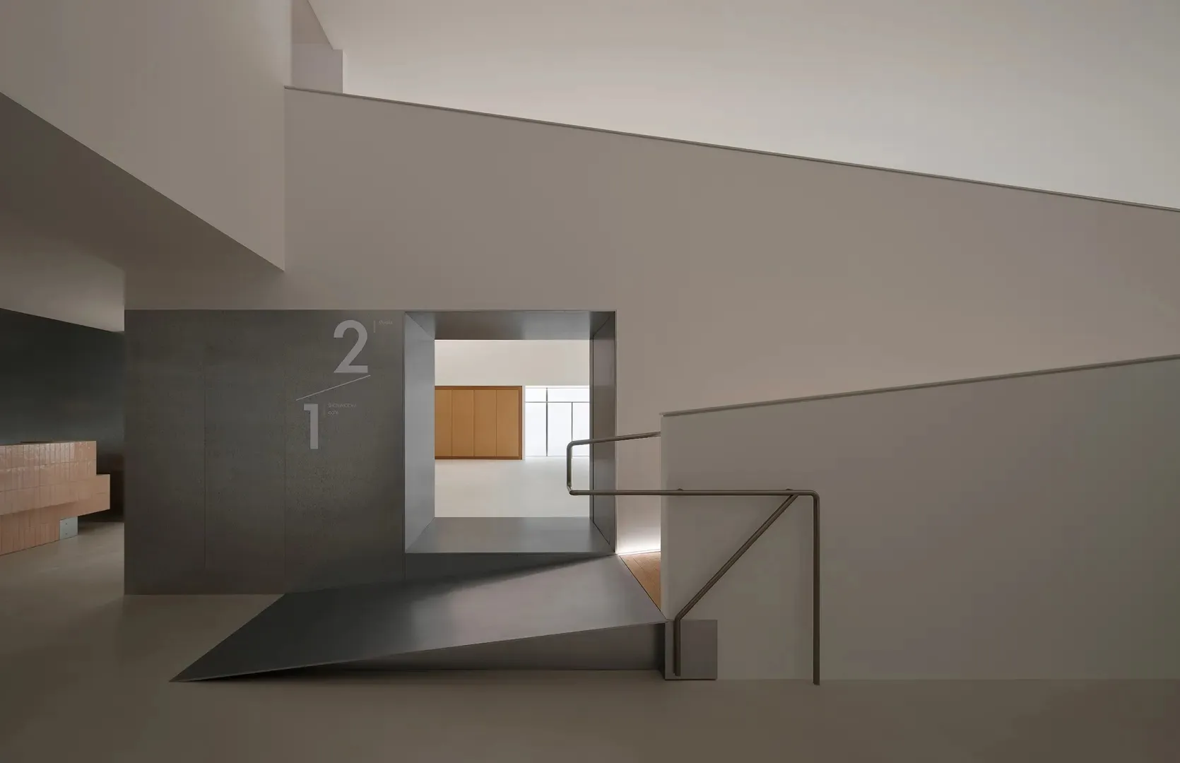 Top-down view of a minimalist concrete staircase with metal handrail leading to a lower level featuring a floating light-oak cabinet against a bright window.