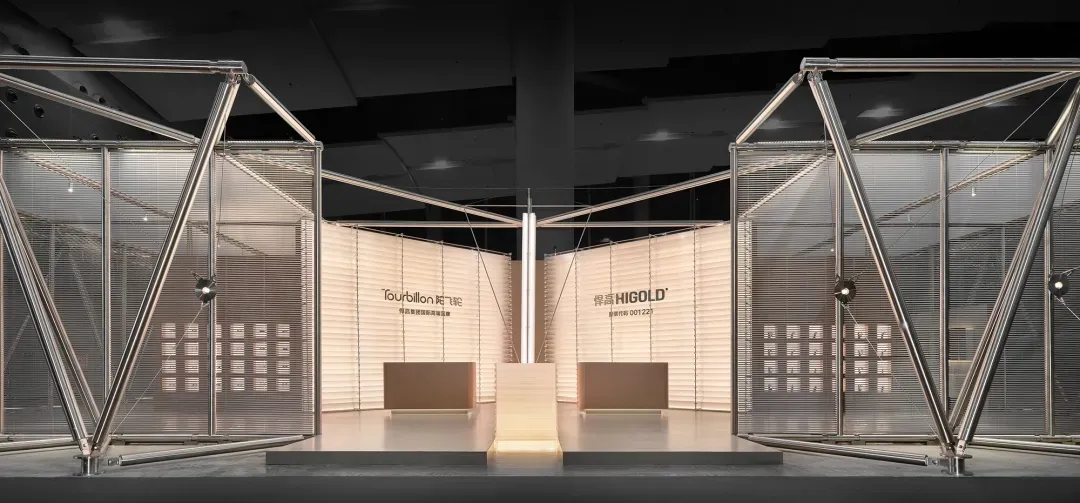 Modern exhibition booth featuring large triangular stainless steel frames, sheer mesh screens, and illuminated central display platforms with brand signage for Higold and Tourbillon.