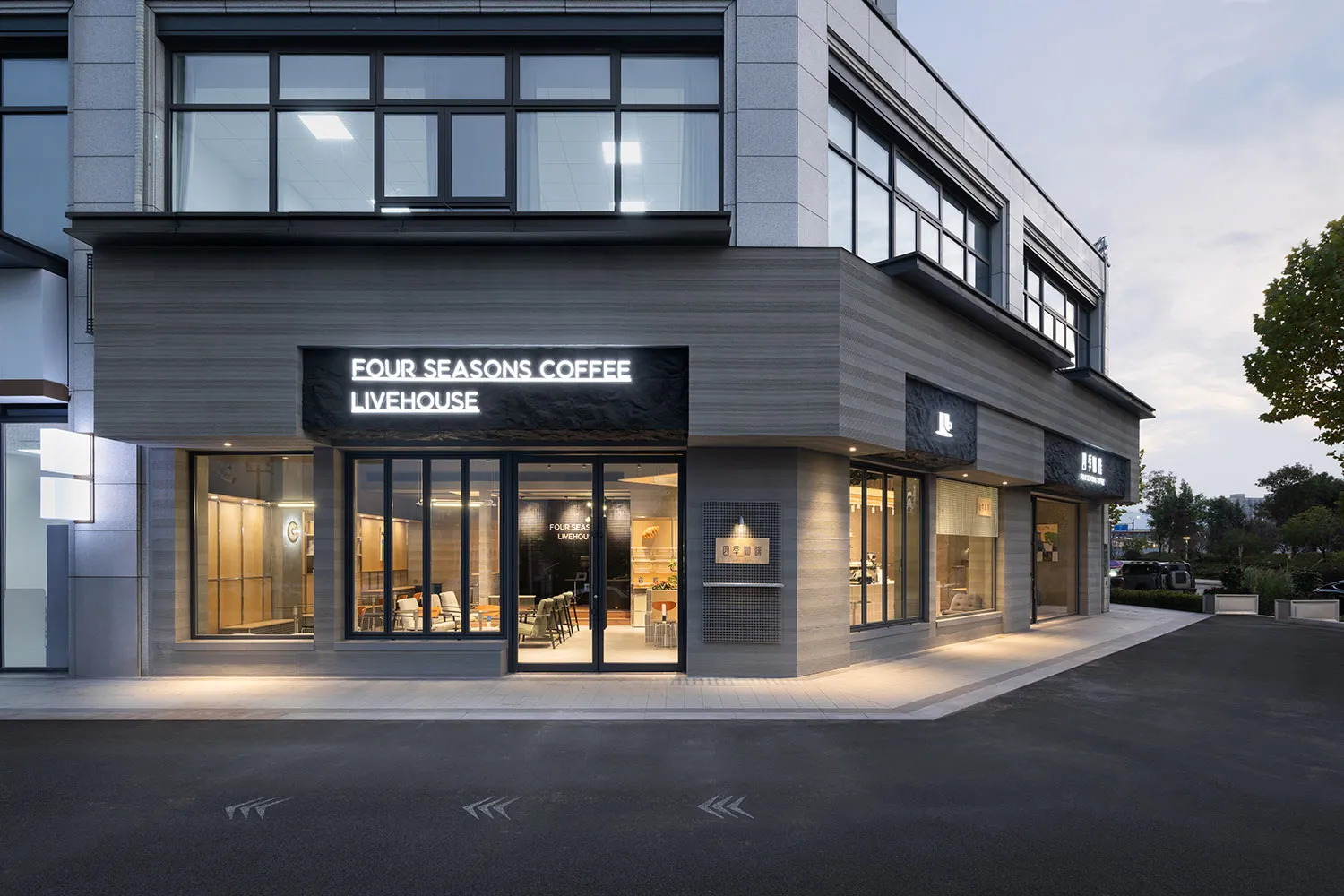 Modern coffee shop exterior with horizontal grey wood cladding, large glass windows, and illuminated signage for Four Seasons Coffee Livehouse at dusk.