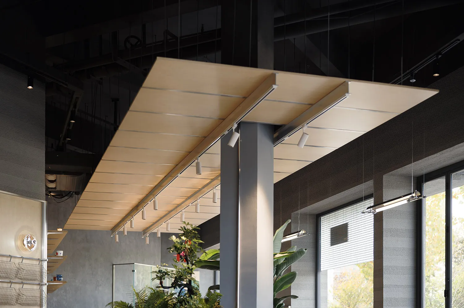 現代工業風室內空間,設有大型懸吊夾板天花板 canopy,整合線性軌道燈,搭配清水模牆面與室內植栽。