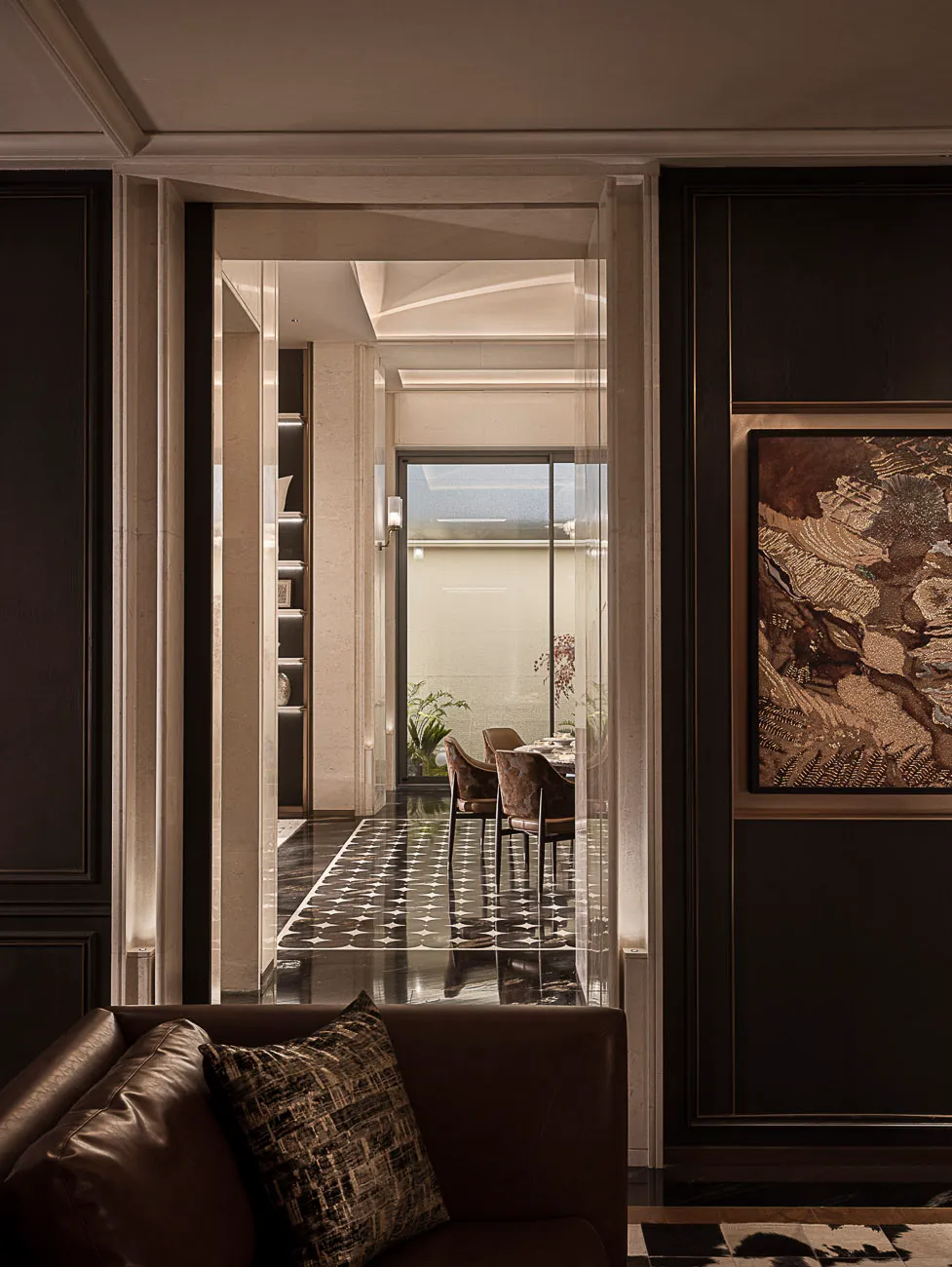 View from a dark brown leather sofa into a luxurious dining room with black and white patterned marble floor, velvet dining chairs, and large abstract artwork.