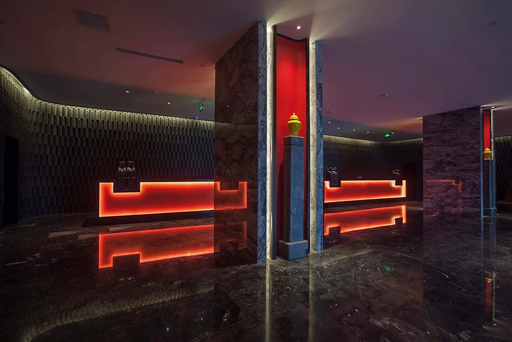 Luxurious hotel lobby interior with dark marble floors and walls, illuminated red reception desk, and dramatic architectural lighting.
