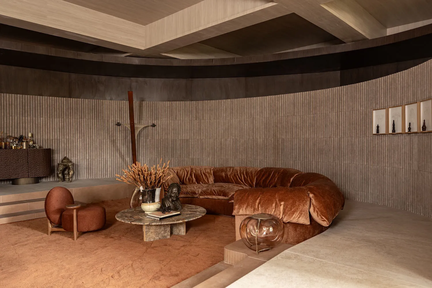 Modern living room featuring a large curved terracotta velvet sofa, marble coffee table, and curved wooden walls with warm earthy tones.