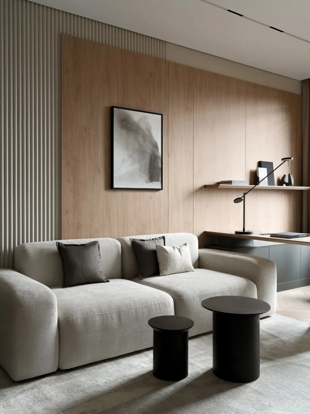 Modern minimalist living room featuring a light beige modular sofa with grey and beige cushions, two black cylindrical side tables, light oak wood wall paneling with vertical slats, and a black-framed abstract artwork.