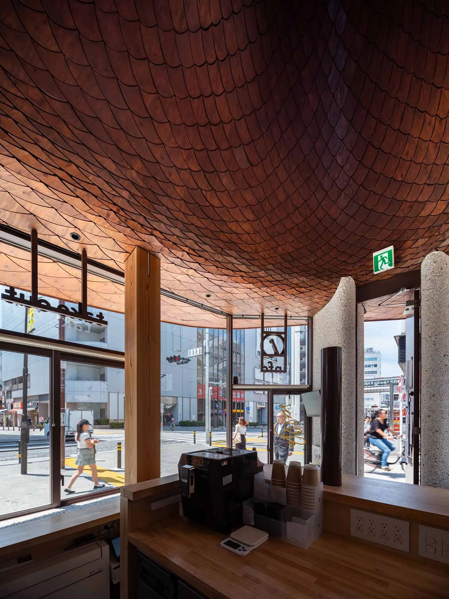 Interior view of a modern Tokyo cafe featuring a dramatic scalloped wooden ceiling, wooden service counter with coffee equipment, and large street-facing windows.