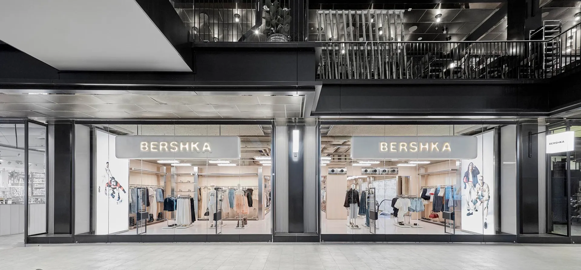 Modern Bershka retail store with full-height glass facade, black metal framing, and illuminated signage in a contemporary shopping mall.