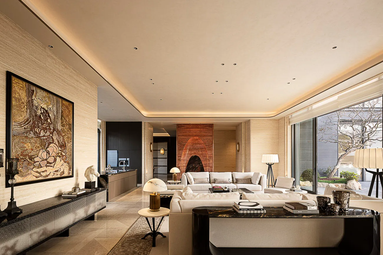 Spacious modern luxury living room featuring full-height travertine walls, large gold floral artwork, white sectional sofa, black marble coffee table, and views to a garden courtyard.