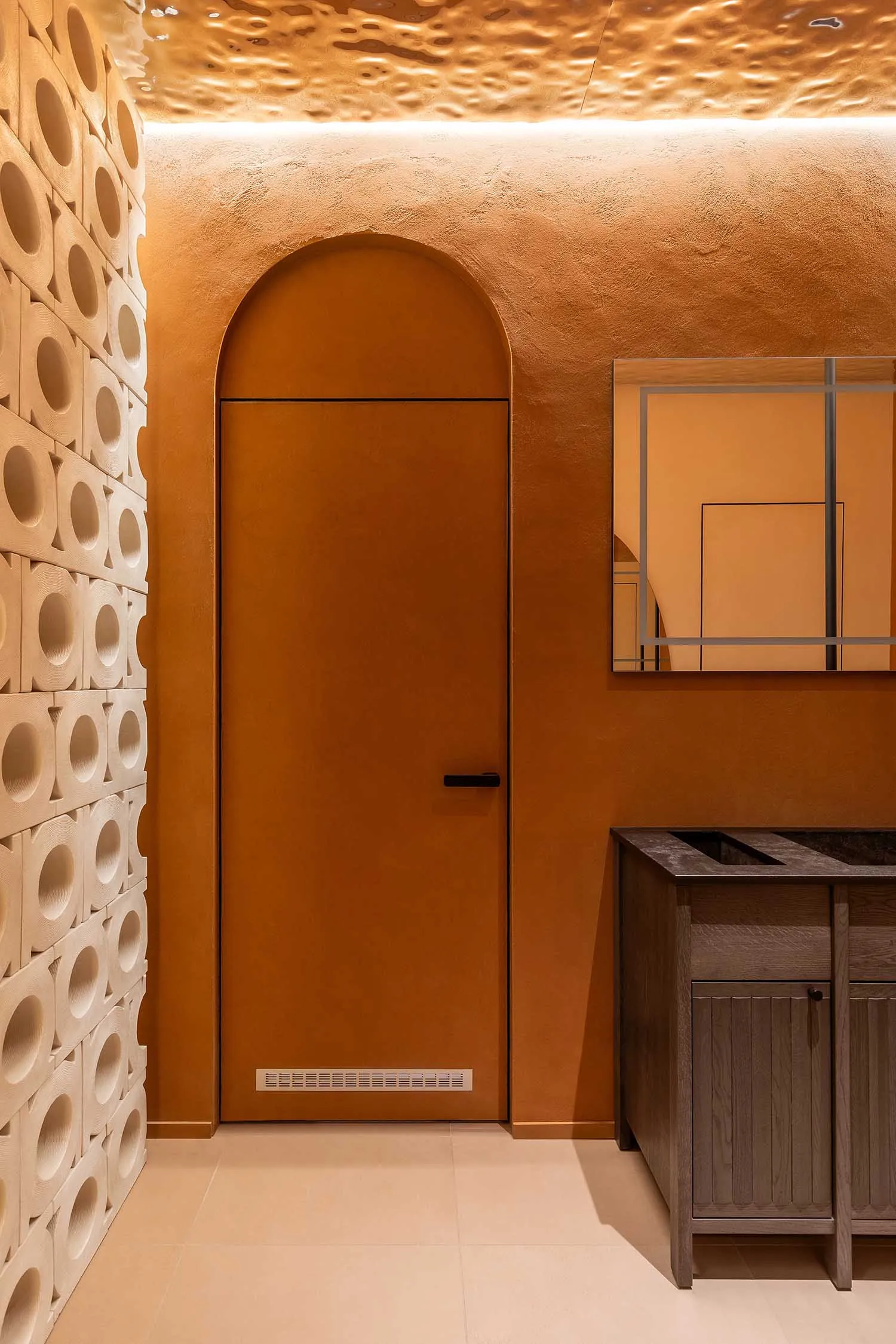 Modern entryway with warm terracotta plaster walls, arched doorway, white 3D circular tile feature wall, wooden vanity, and textured golden ceiling.