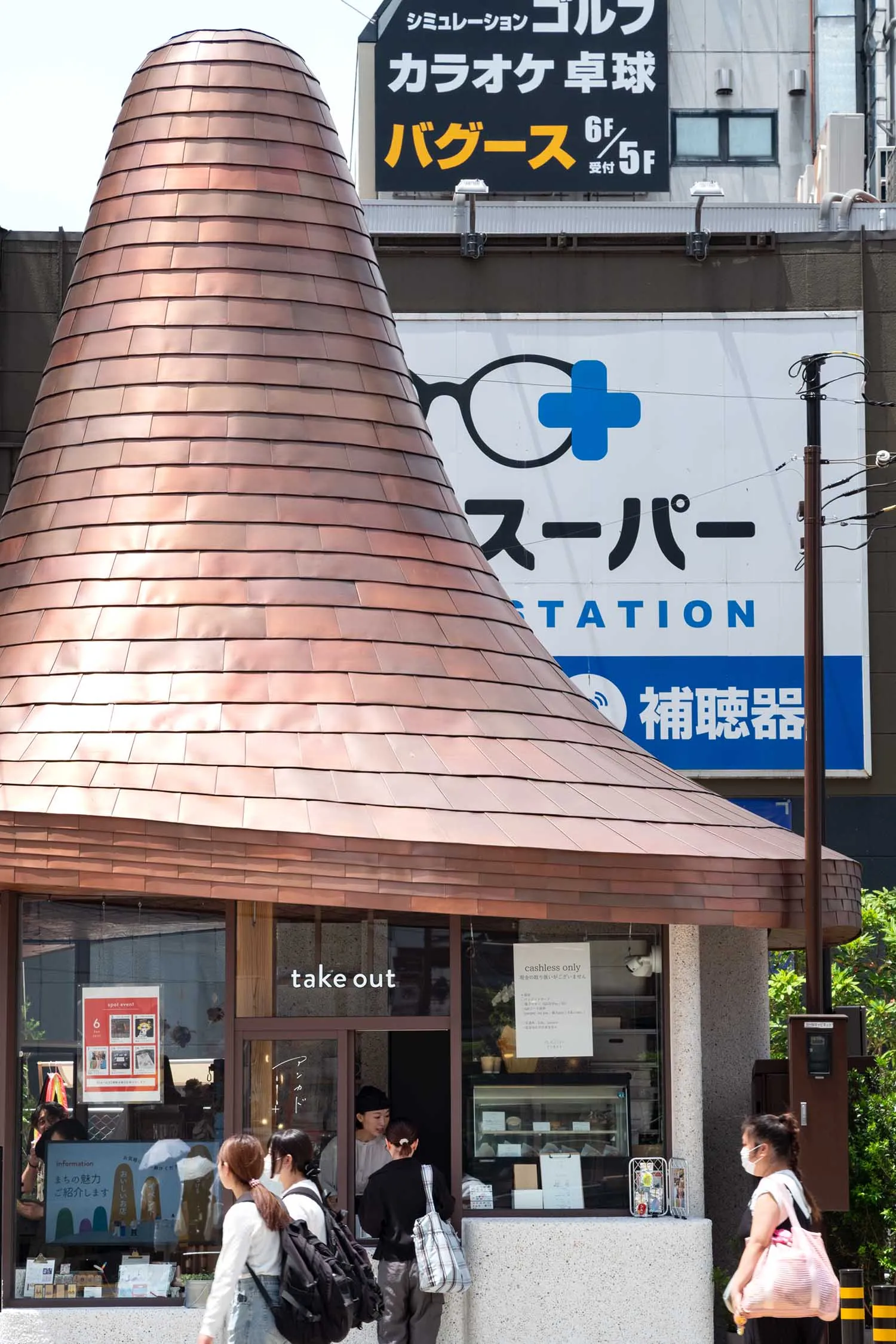 街景中一座小店擁有醒目的大型銅製圓錐屋頂,表面覆蓋交疊的銅瓦,前方有行人經過,背景可見商業招牌。