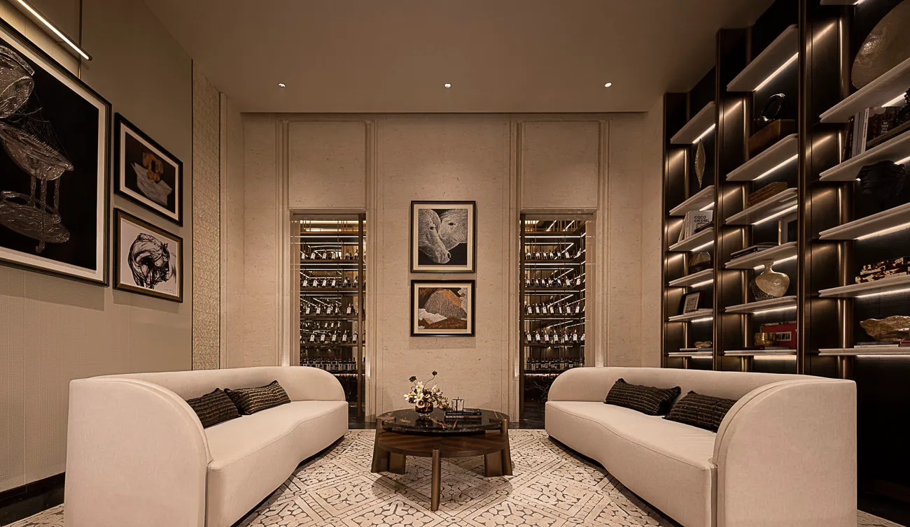 Modern luxury living room with two curved cream sofas, dark marble coffee table, patterned rug, and illuminated wine cellar display cases built into the back wall.