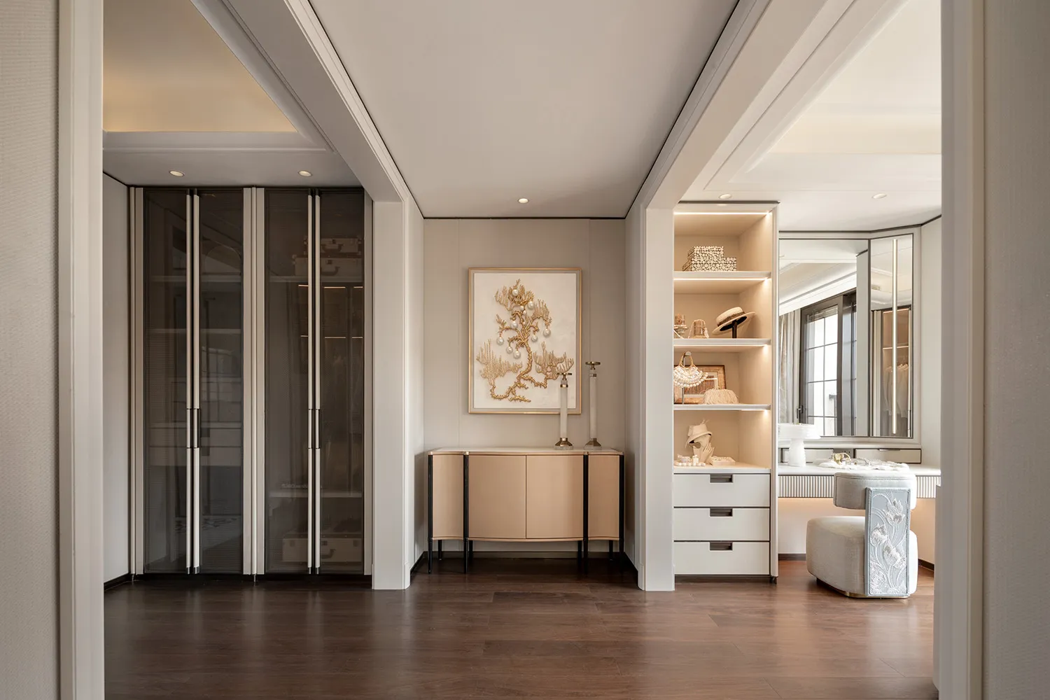 Modern luxury walk-in closet with neutral beige and white cabinetry, dark oak flooring, built-in LED lit display shelves, and a large framed golden coral artwork.