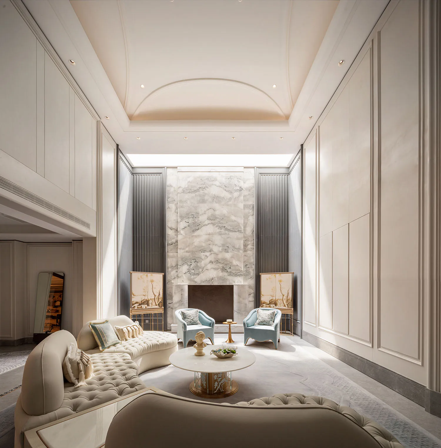 Elegant luxury living room featuring a large curved ivory tufted sofa, two light blue armchairs, a round marble coffee table, and a dramatic marble fireplace wall under a high coffered ceiling.