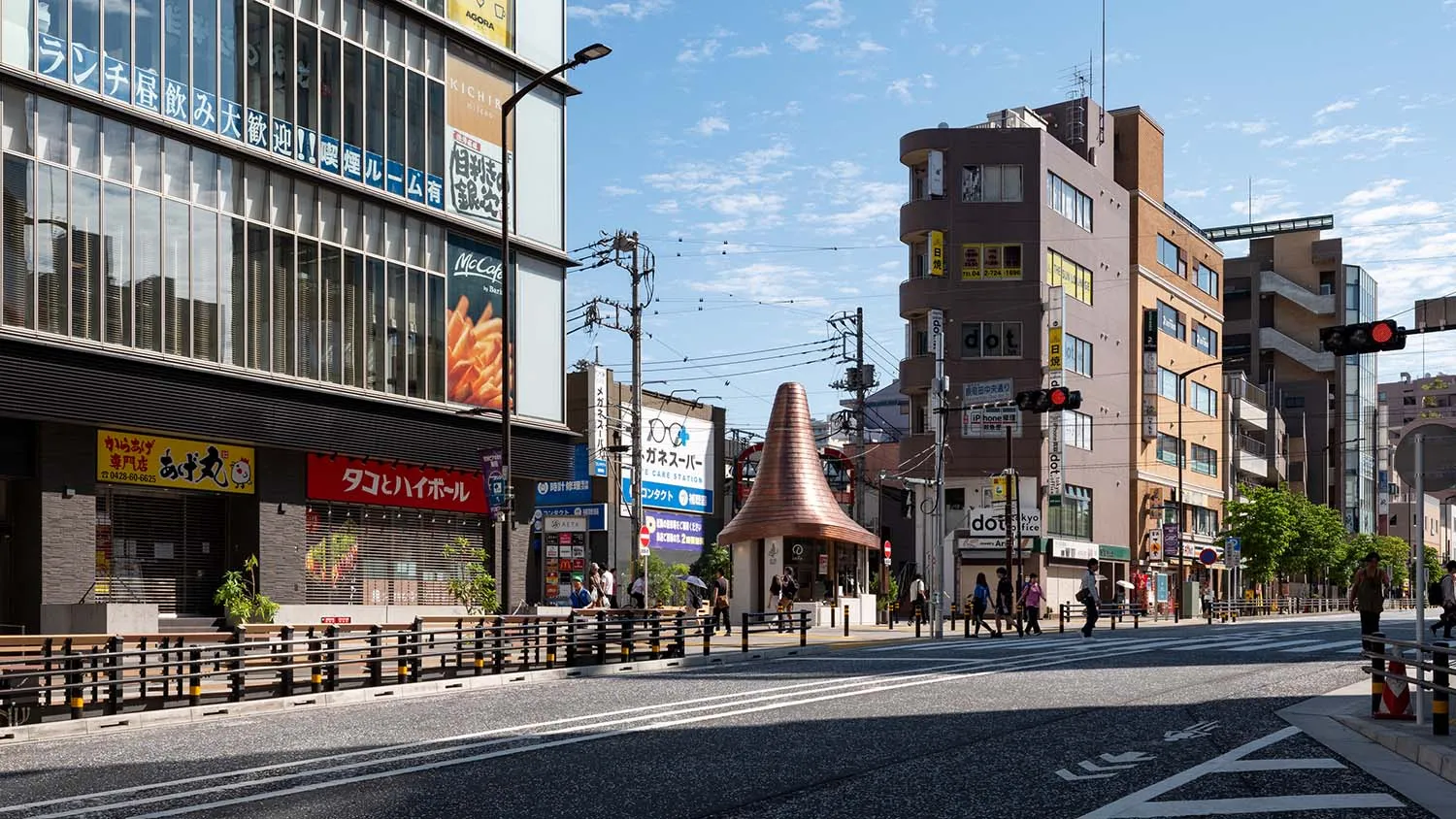 晴朗白天日本熱鬧商業街景,兩旁林立商店、日文招牌、行人、交通號誌,以及中央醒目的銅色圓錐形小亭。