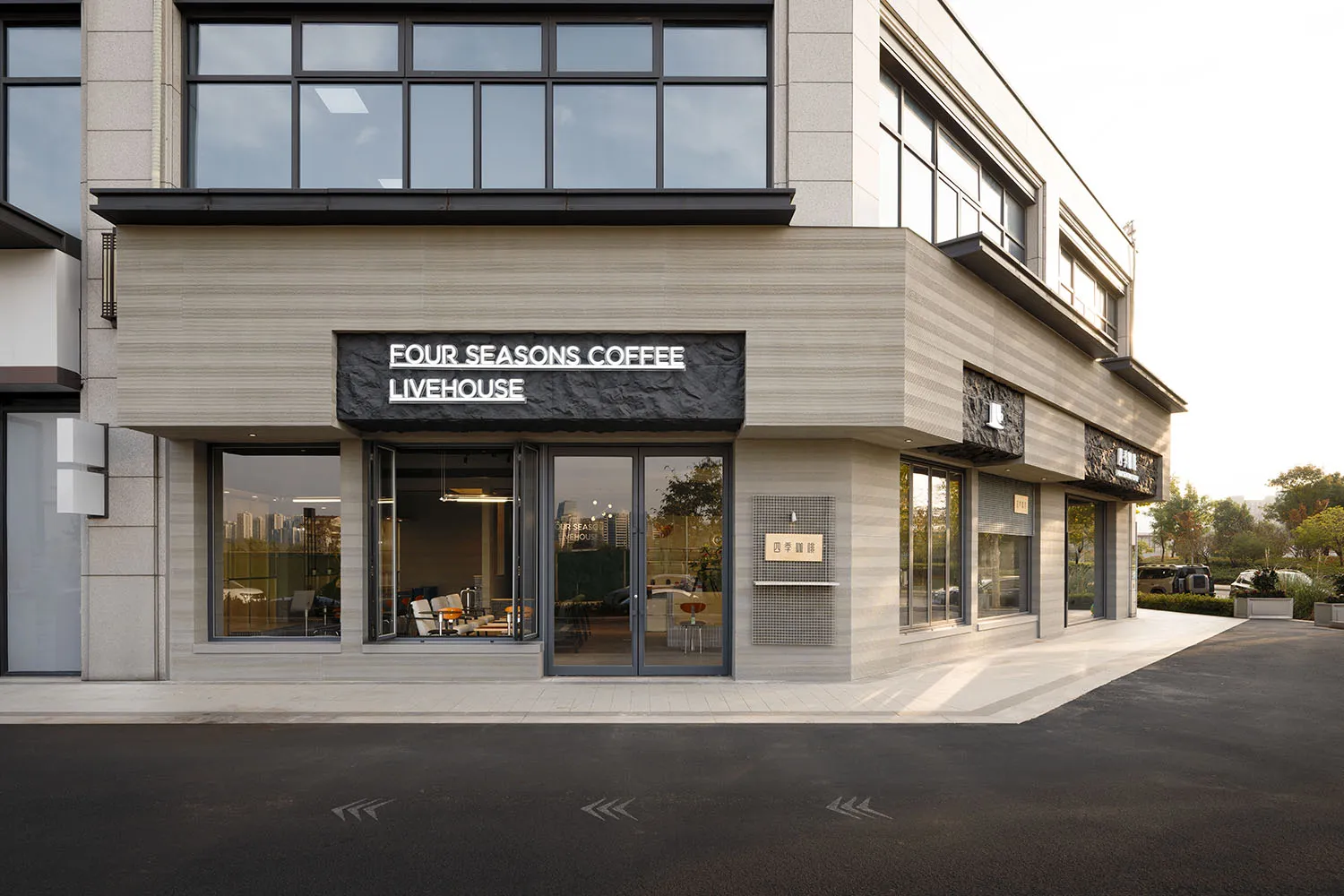 Modern corner commercial building with horizontal travertine stone cladding, large glass windows, and black textured signage for Four Seasons Coffee Livehouse.