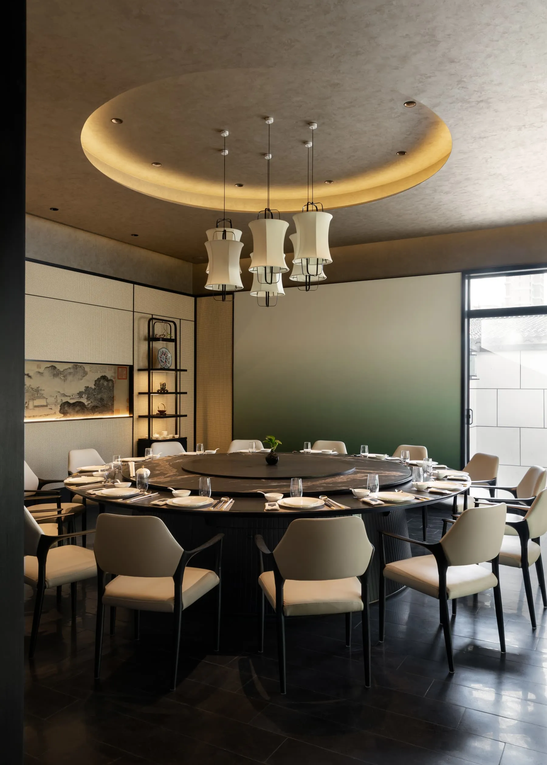 Elegant modern Chinese dining room with a large round black marble lazy-Susan table, cream upholstered chairs, and a striking circular recessed ceiling with pendant lights.