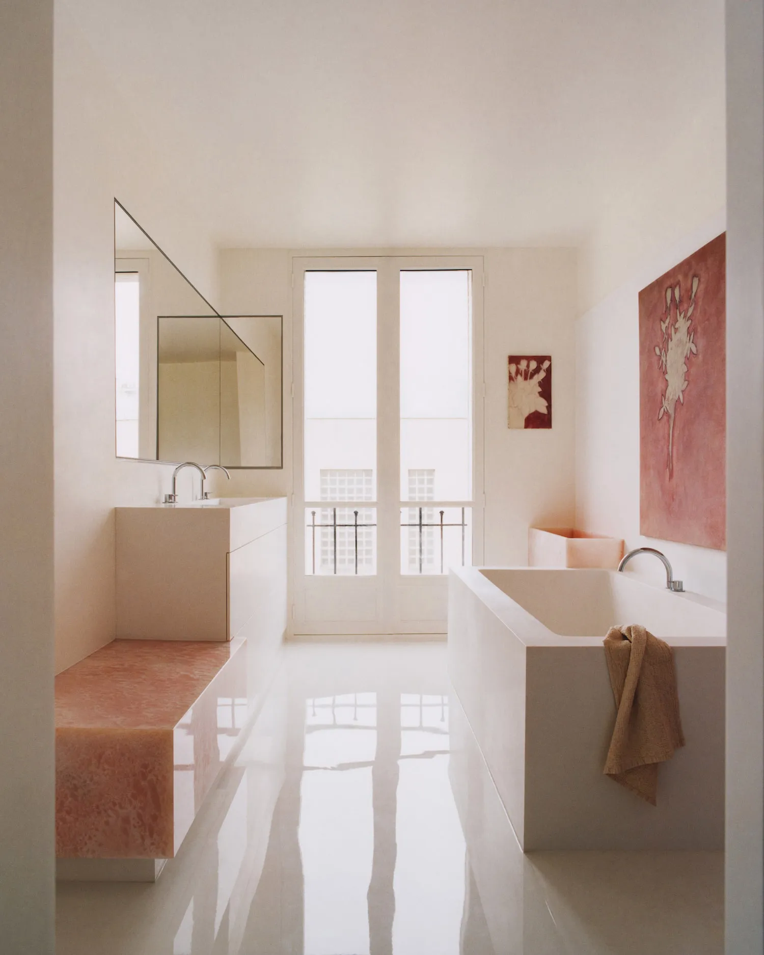 Minimalist bathroom interior with white walls, glossy floor, pink terrazzo bench and bathtub, large mirror, and natural light from glass doors.