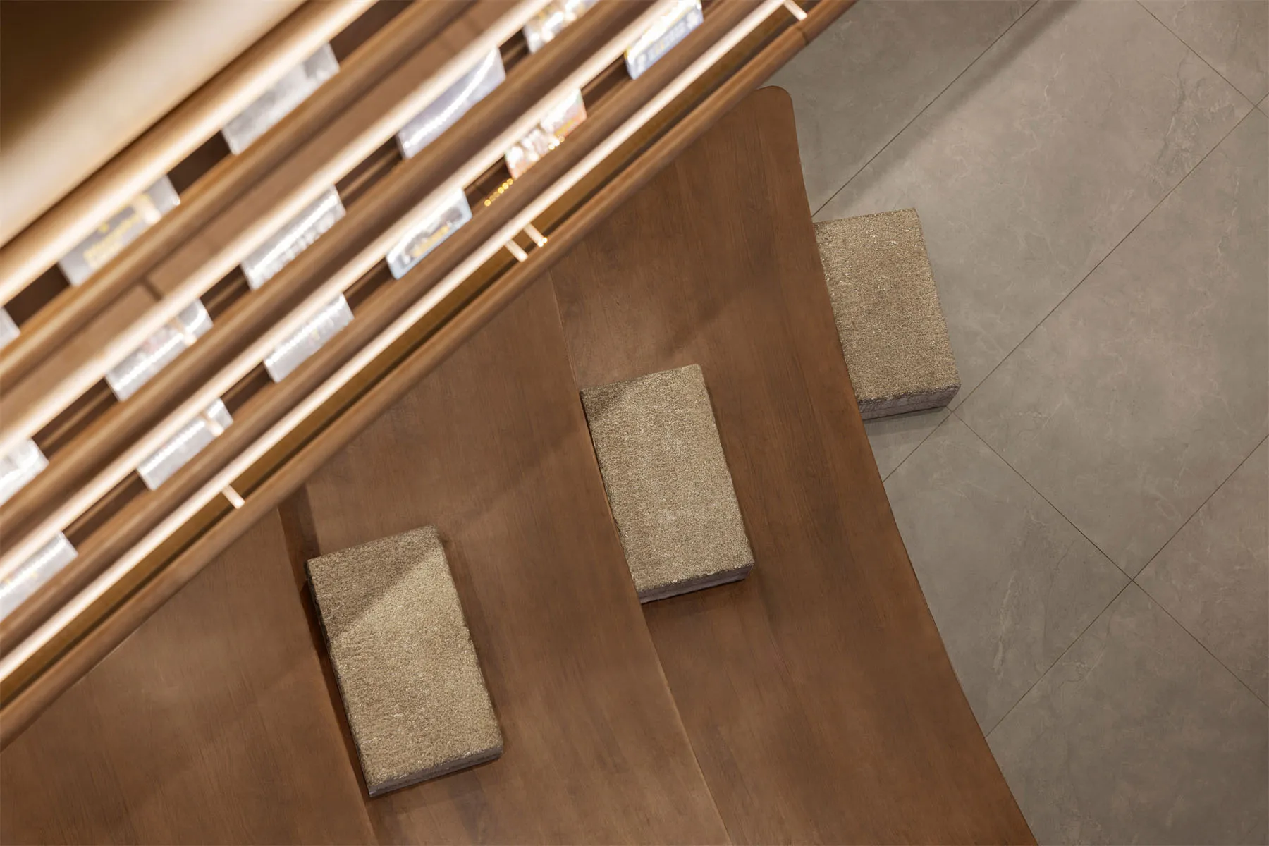Close-up overhead view of a modern wooden staircase featuring warm walnut steps and textured stone treads, with integrated LED lighting along the handrail.