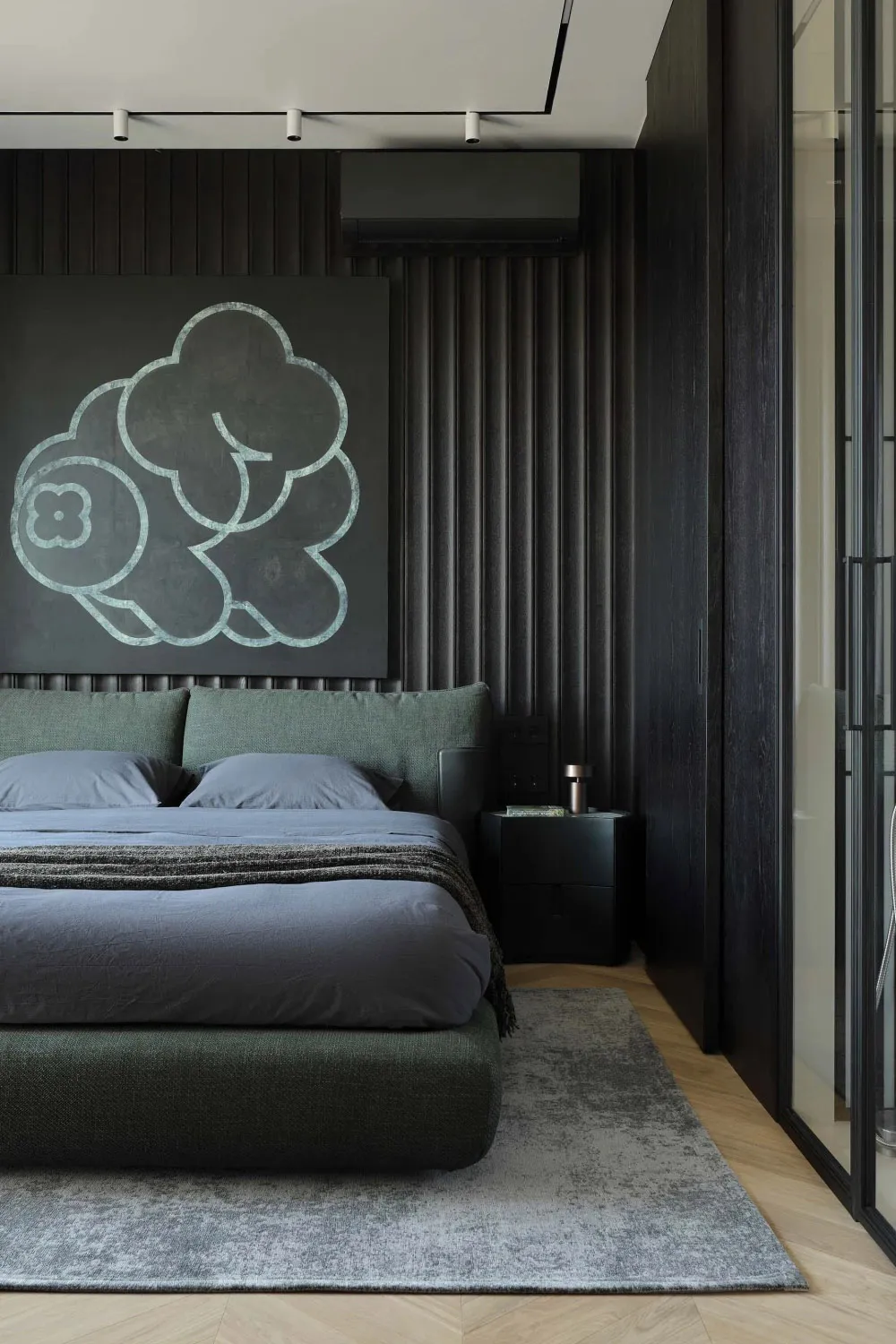 Modern dark-toned bedroom with sage green upholstered bed, large cloud-shaped artwork in teal on black wall, wood herringbone floor and grey area rug.