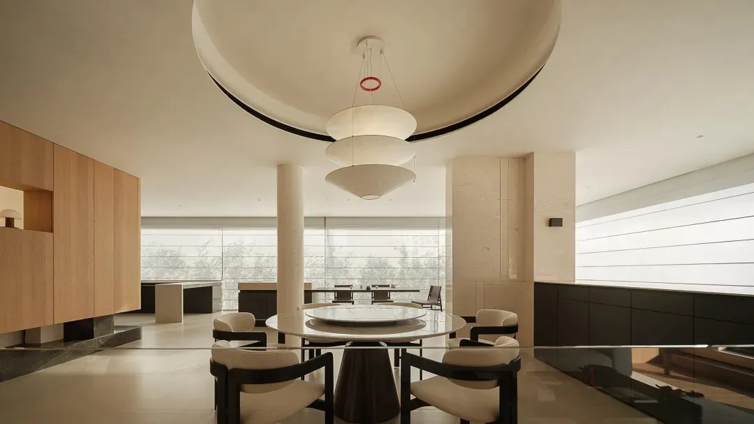 Modern luxury dining room featuring a large round white marble table, four upholstered dining chairs with dark wood frames, and a dramatic three-tiered white pendant light hanging from a curved ceiling detail.