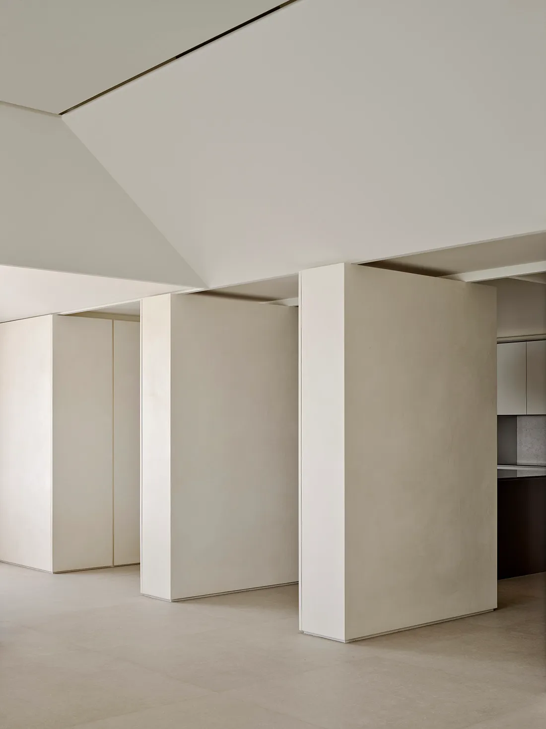 Minimalist living room interior featuring off-white micro-cement walls, a floating partition wall, high ceilings with recessed lighting, and seamless concrete flooring.