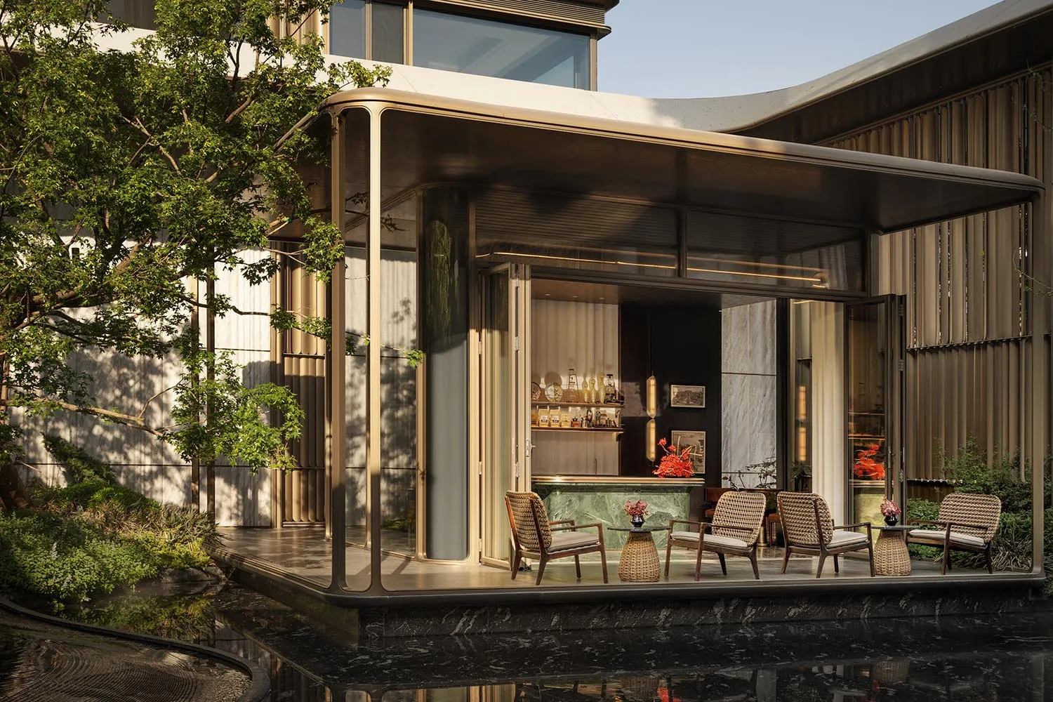 Modern luxury courtyard bar with brass-framed glass pavilion, green marble counter, rattan lounge chairs, and a dark marble reflecting pool surrounded by trees.