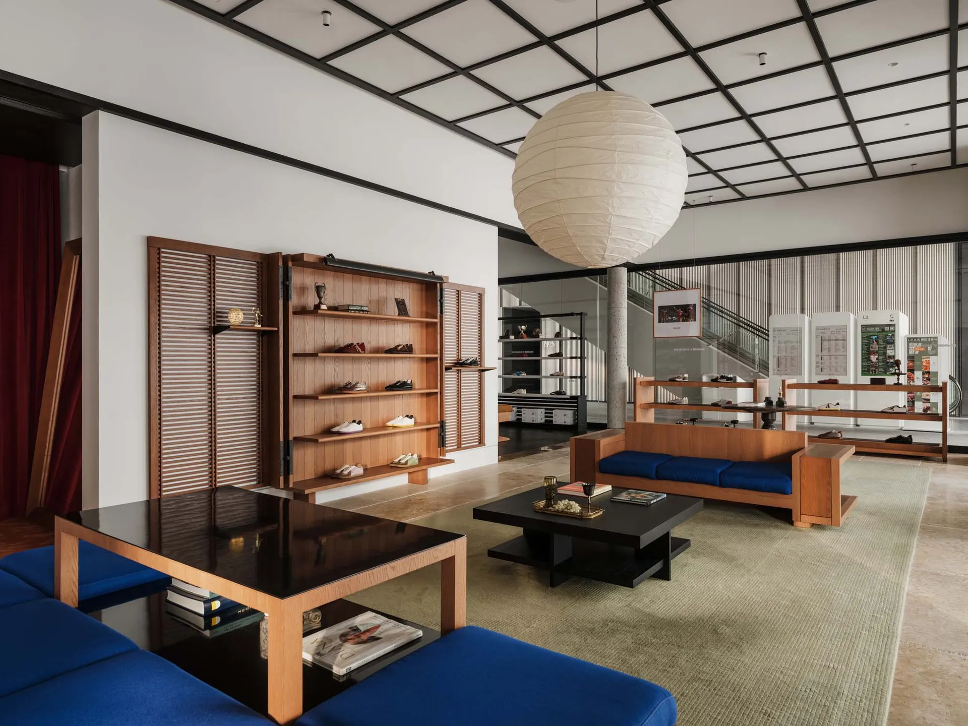 現代鞋店室內空間,設有柚木展示架、藍色沙發、黑色茶几與大型白色紙燈籠吊燈。