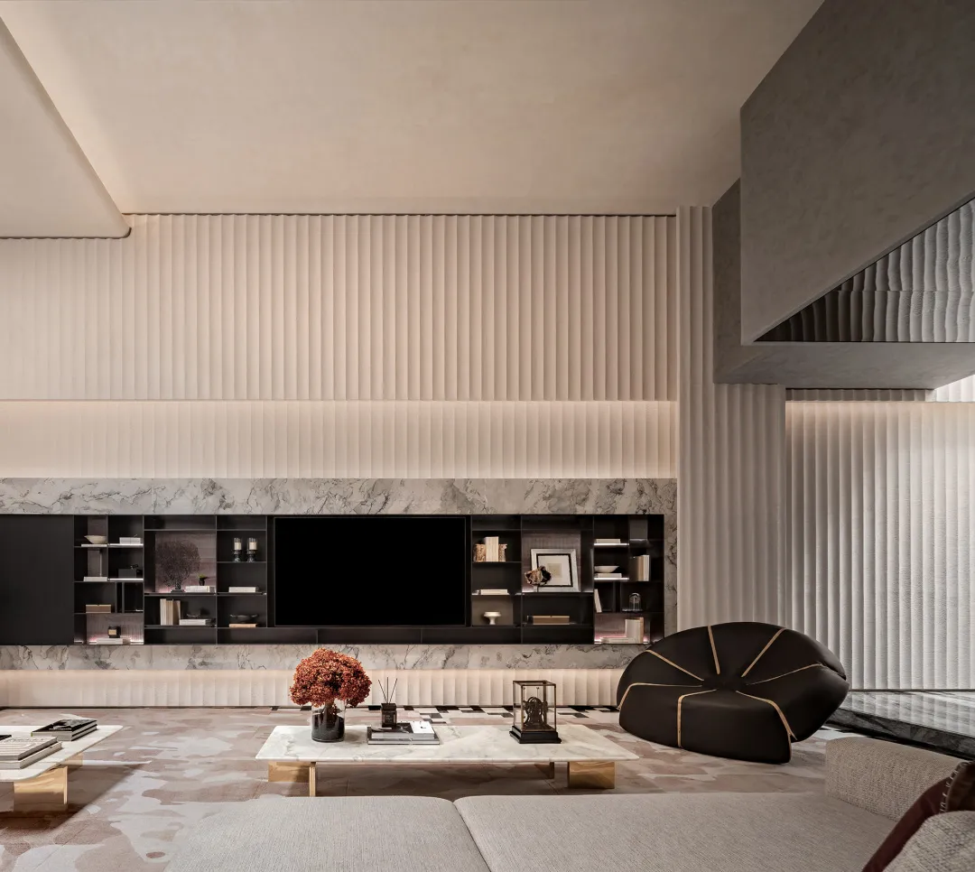 Modern luxury living room with a large black entertainment center set against a white marble wall, vertical fluted beige panels, integrated LED lighting, a sculptural dark brown leather ottoman, and a marble coffee table.
