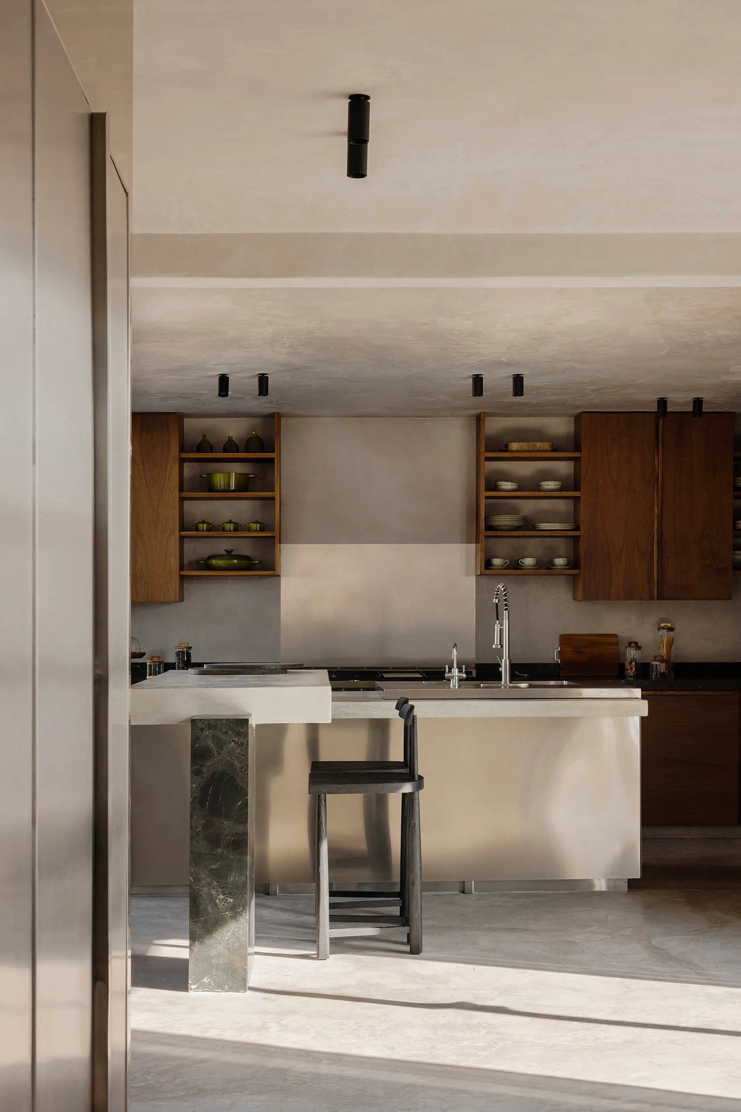 Modern minimalist kitchen featuring a concrete island with dark green marble support, walnut open shelving and cabinetry, black faucet, and concrete floor.