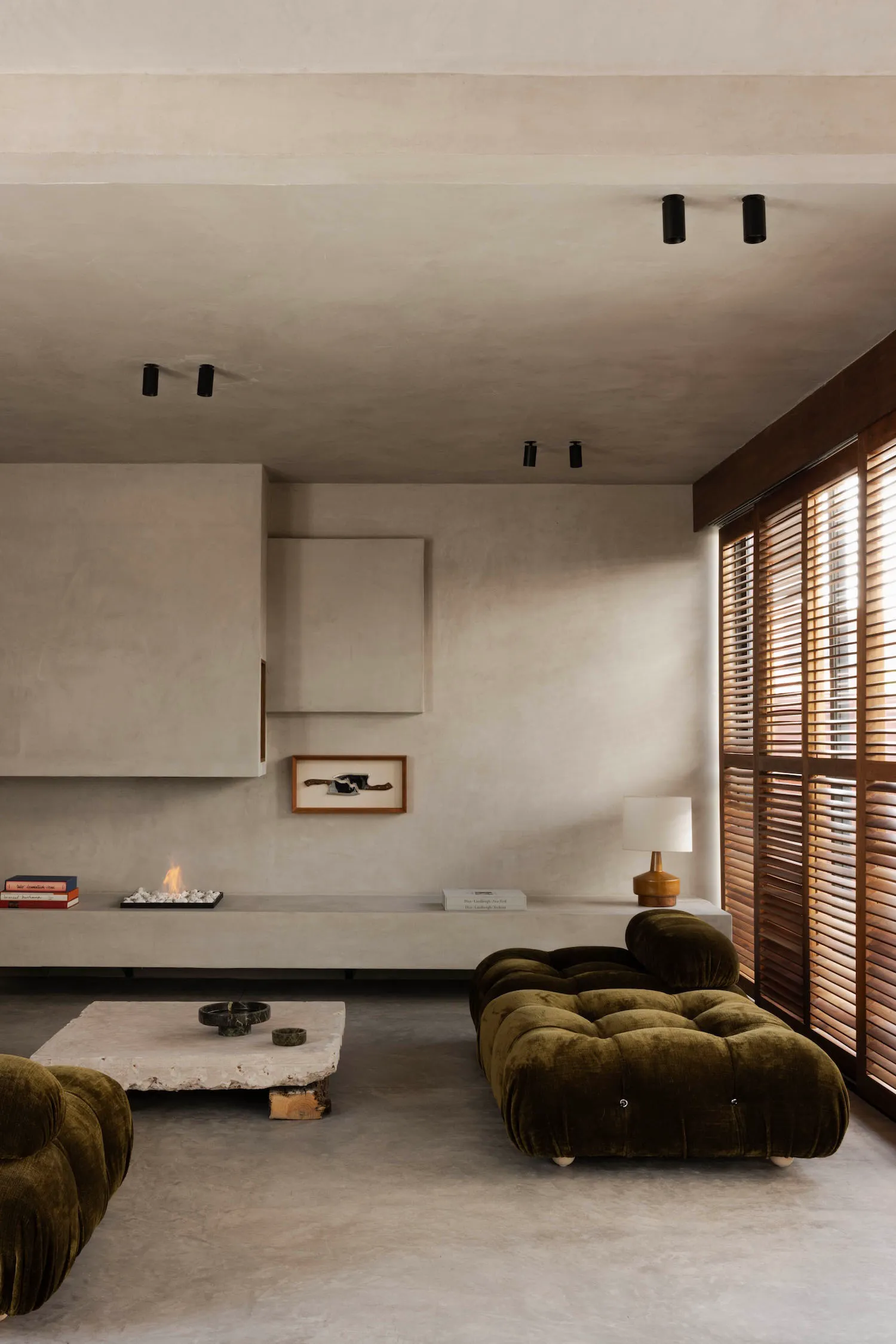 Modern minimalist living room with olive green velvet tufted cloud sofa, raw concrete walls, floating console, and stone coffee table.
