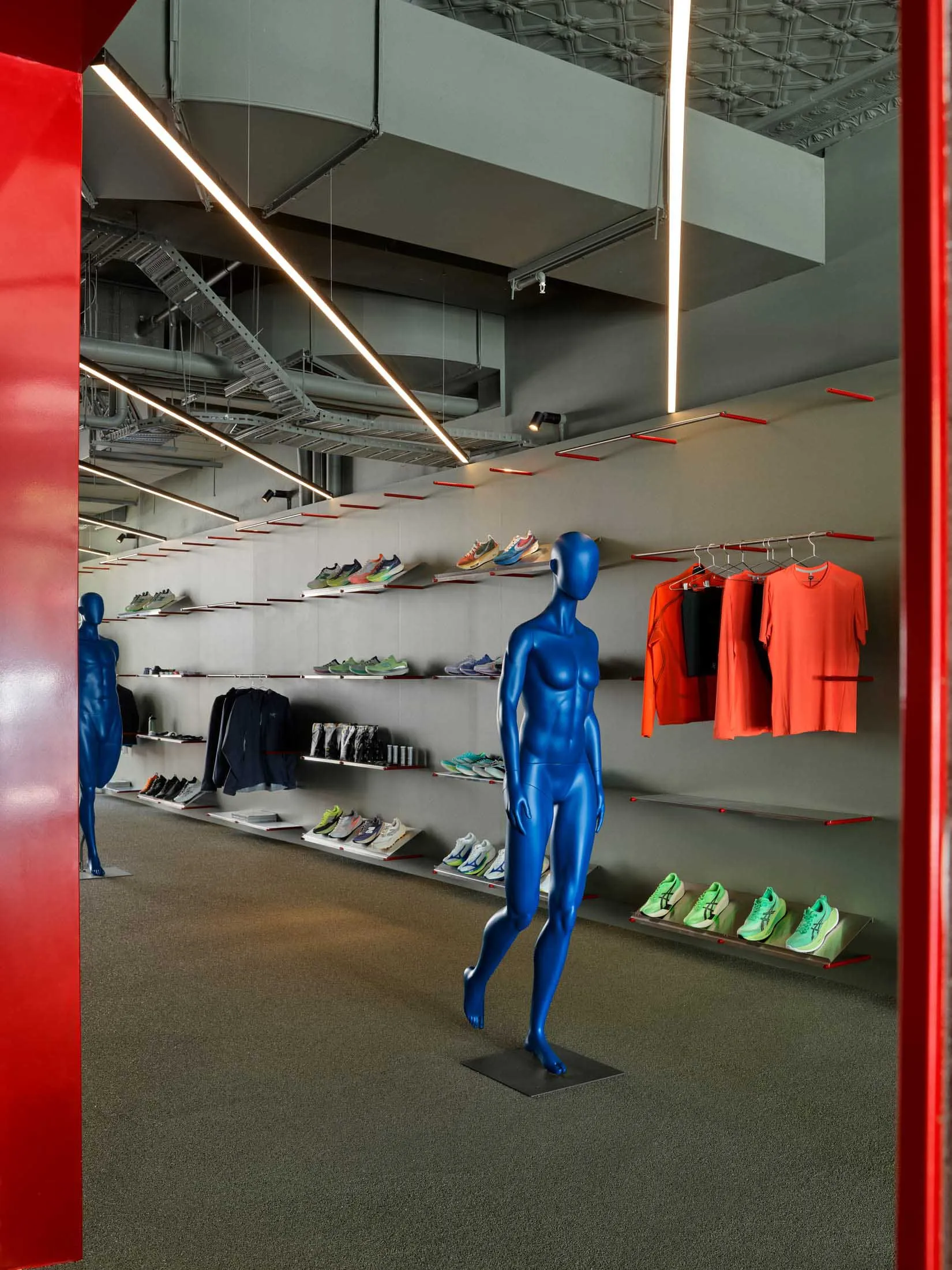 現代運動服飾店內部,展示亮藍色光澤人體模型、牆面陳列架上擺放彩色運動鞋、懸掛運動服,以及戲劇性的線性LED燈光。