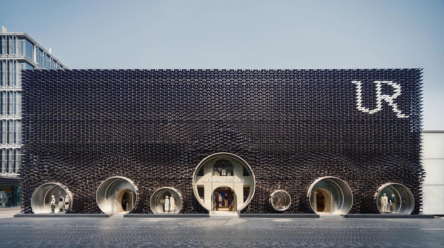 Front view of Urban Revivo flagship store in Taipei featuring a massive black textured façade made of recycled plastic tiles and multiple circular tube-shaped entrances with mannequins displayed inside.