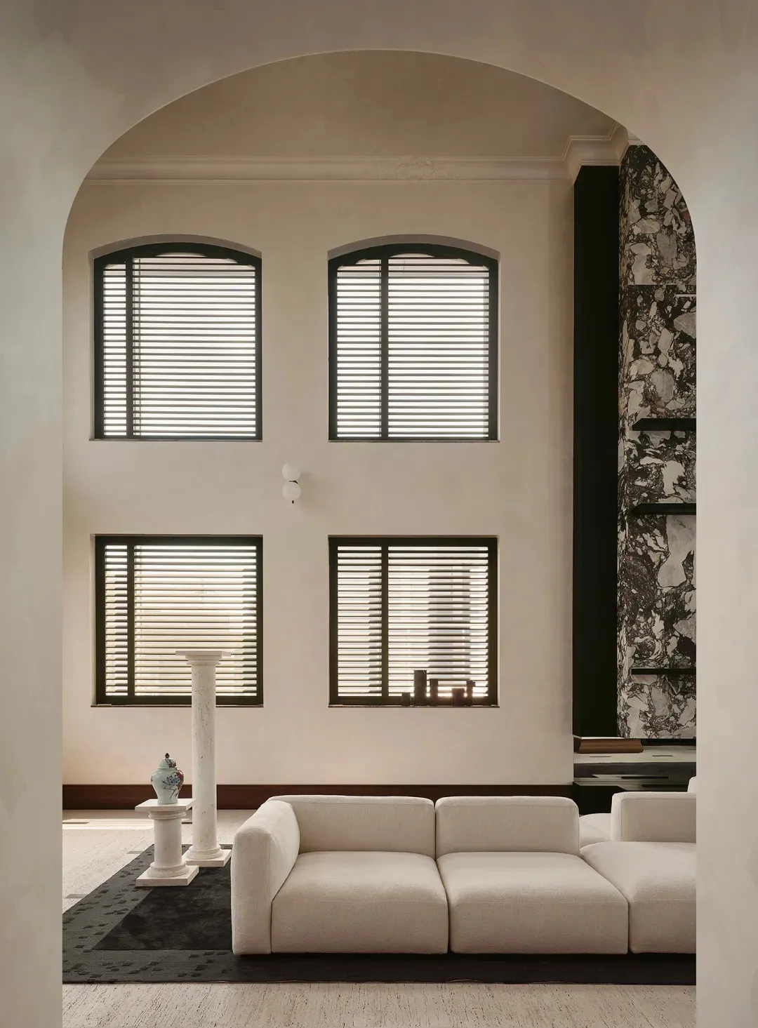 Modern minimalist living room featuring a large arched entryway, off-white modular sofa, dark marble accent wall, and four arched windows with black blinds.