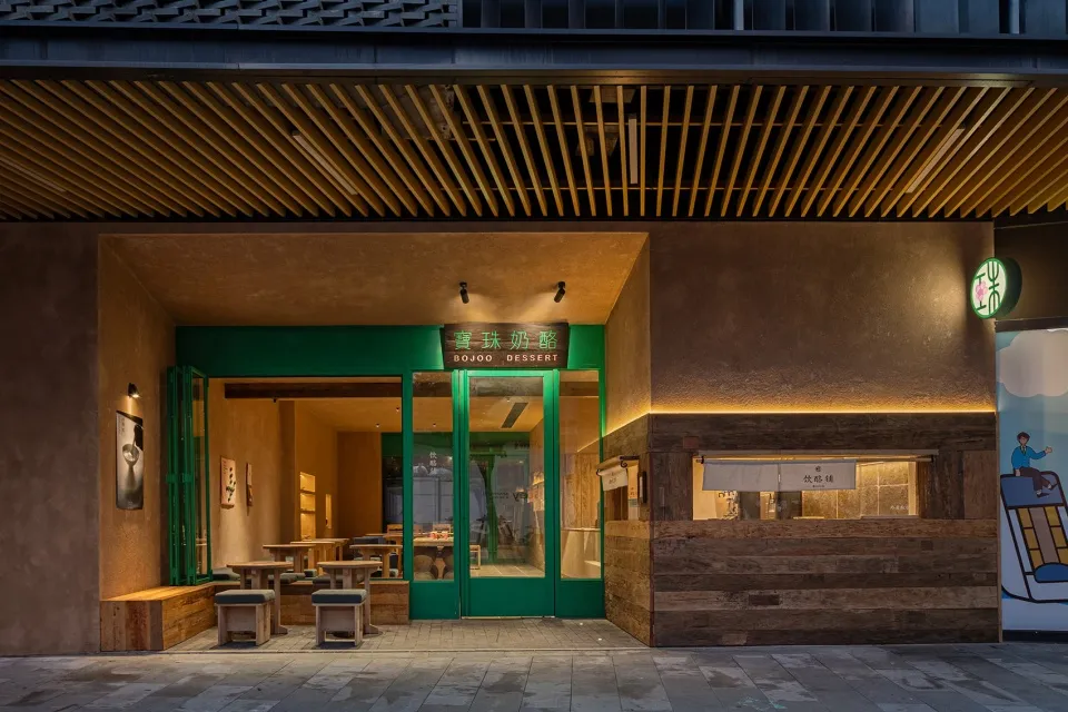 Night view of a modern dessert shop entrance with green doors, wooden counter, concrete walls and warm lighting in Taiwan.