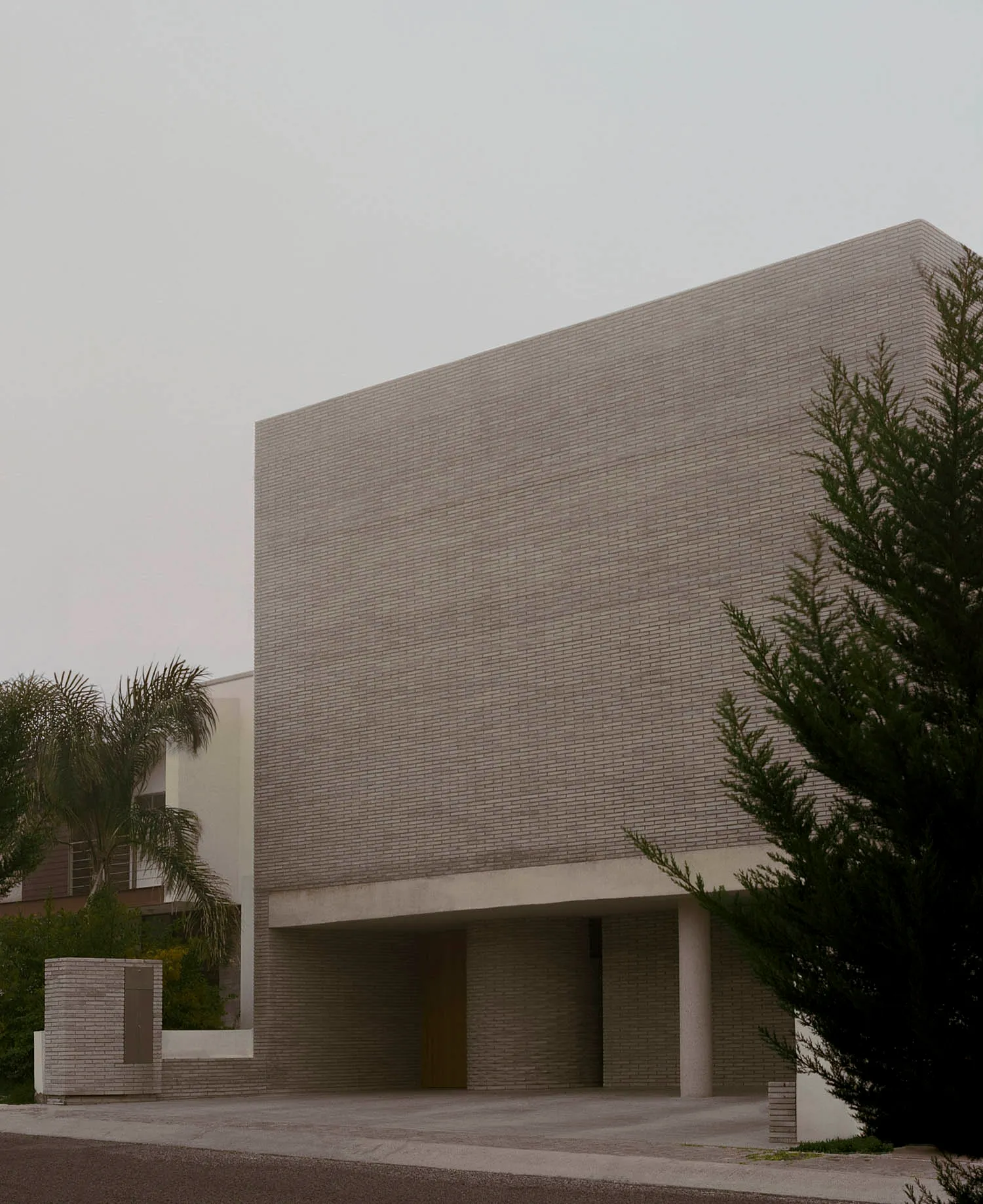 Exterior view of a brutalist concrete brick building with a large overhanging rectangular volume and wooden entrance door.