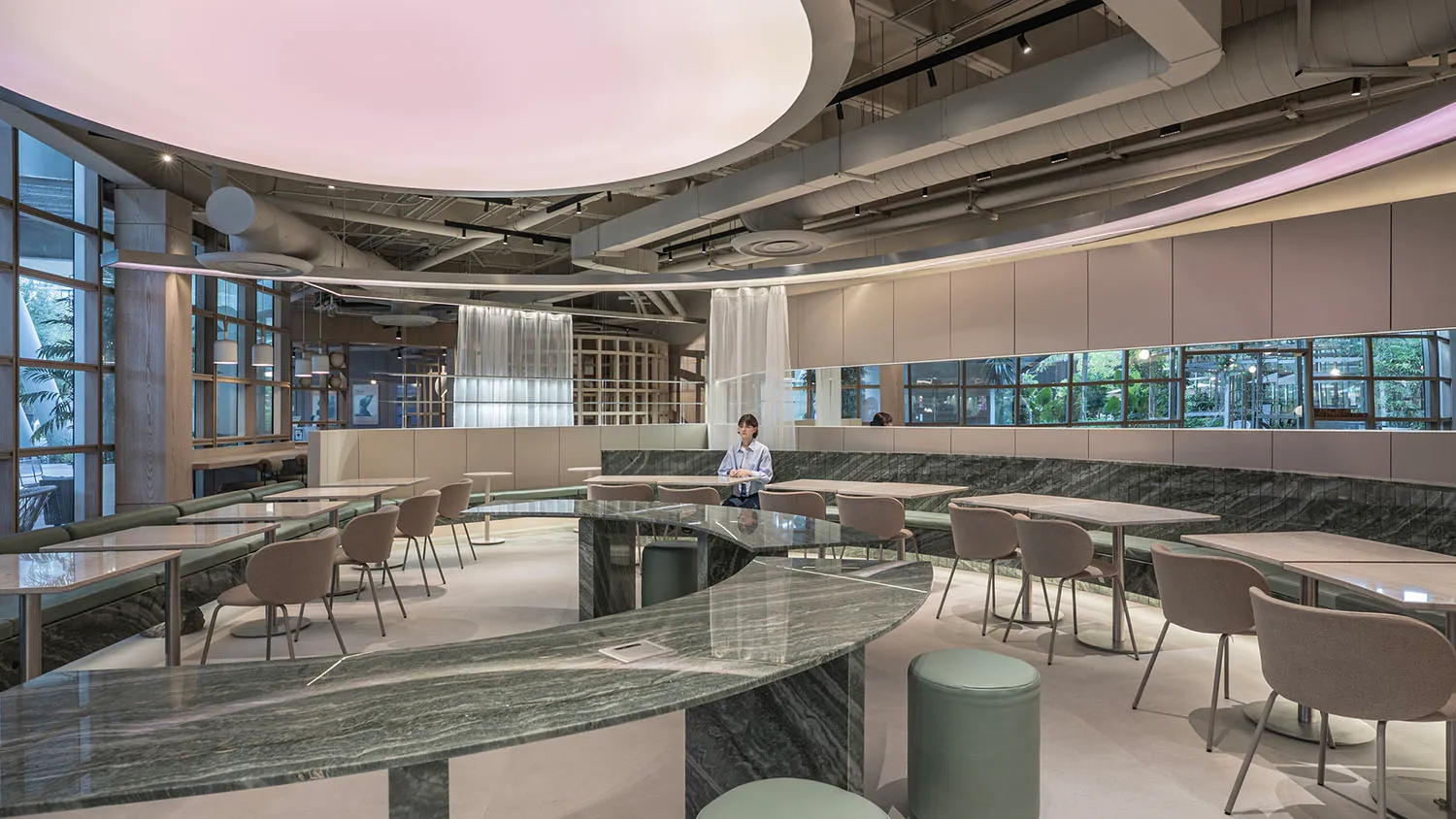 Modern restaurant interior featuring a large curved green marble counter, upholstered dining chairs, built-in banquettes, and dramatic circular pink ceiling light panels.