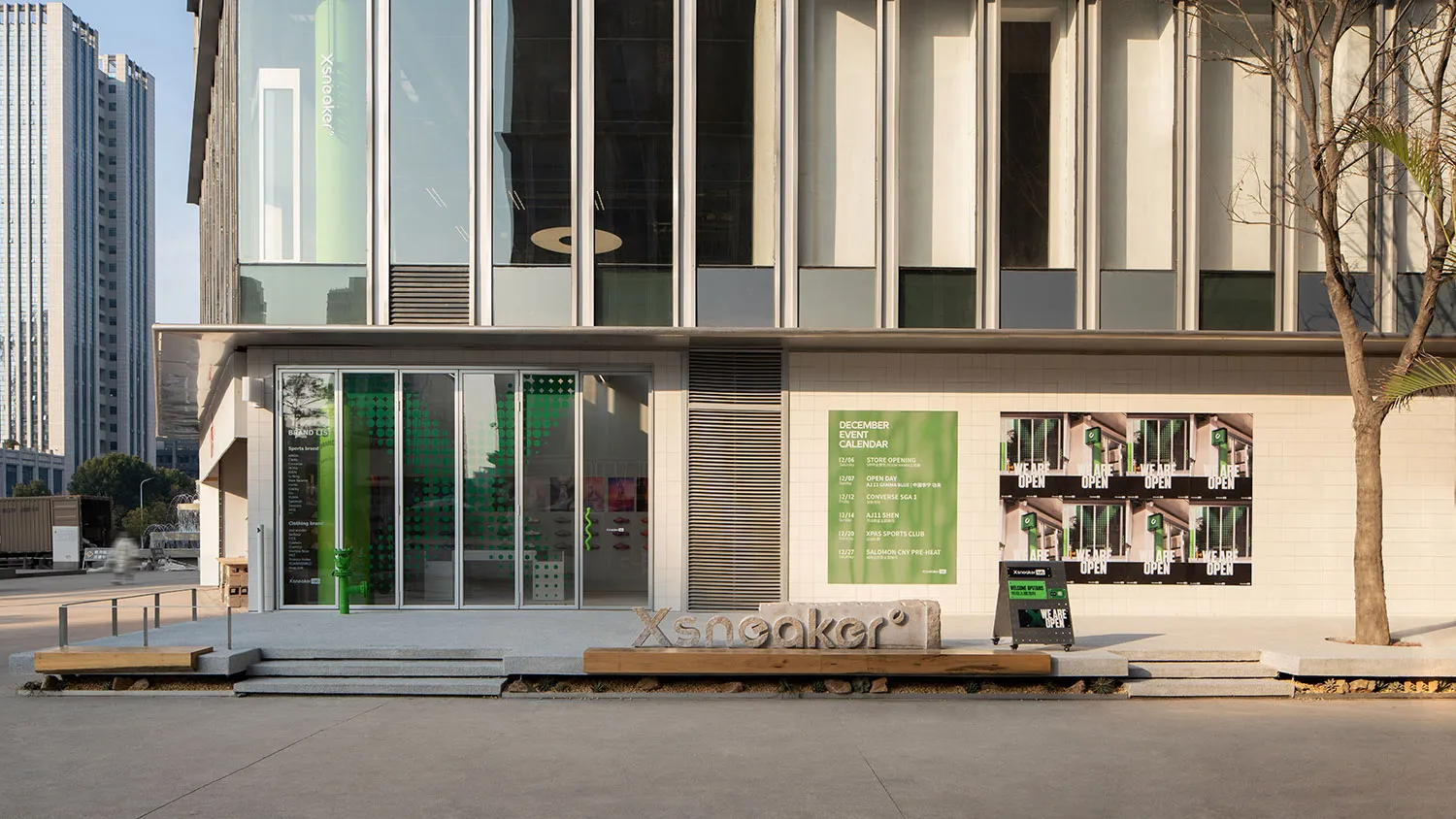 Exterior view of a modern Xsneaker retail store featuring a full-height glass facade, white tiled lower walls, concrete steps, and prominent green branding elements.