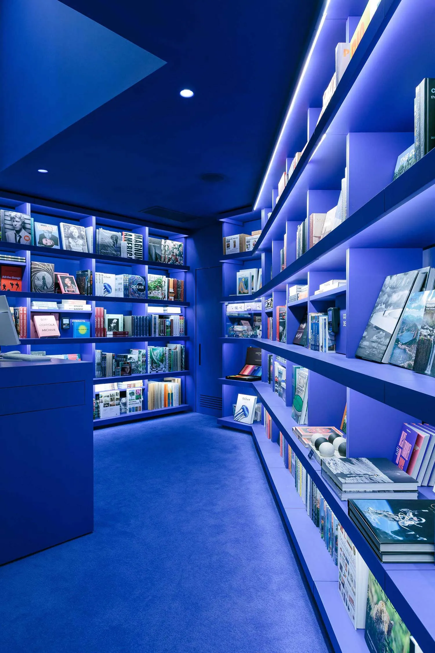 Immersive monochromatic blue library room with floor-to-ceiling LED backlit bookshelves and deep blue carpet.