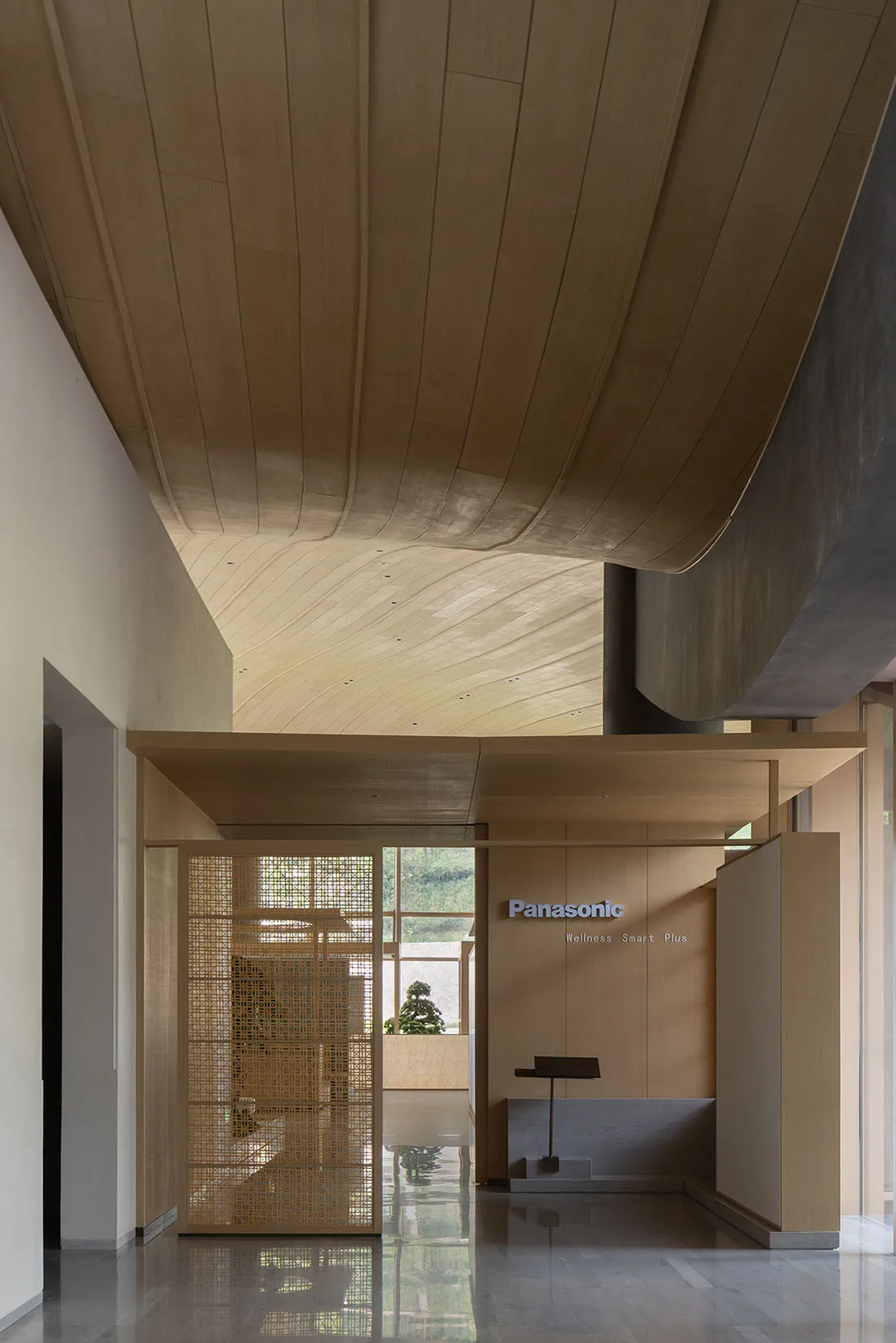 Modern Japanese-style entrance hall with a dramatic curved wooden ceiling, wooden lattice screen, polished concrete floor, and Panasonic wellness display.