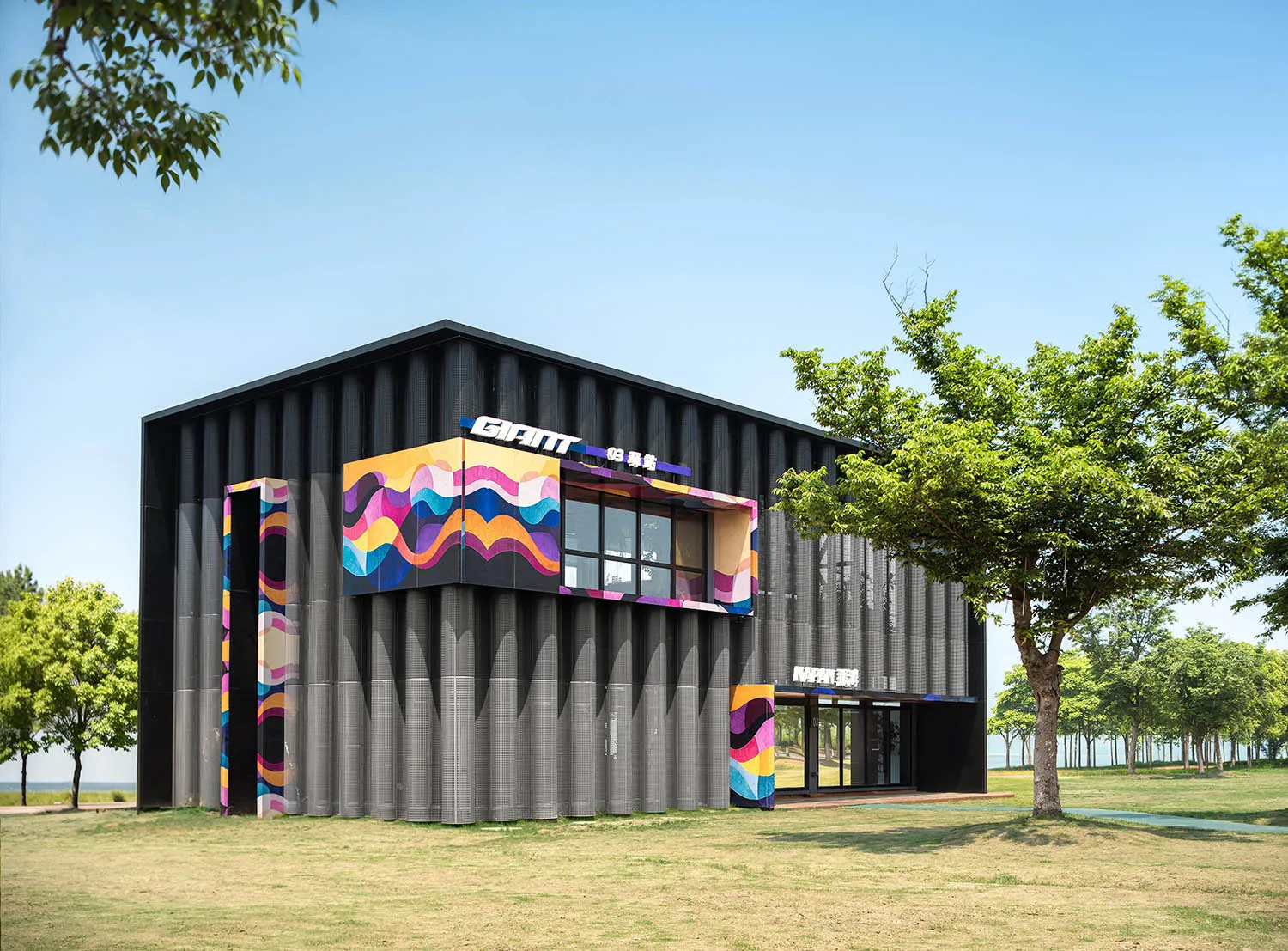 Modern black corrugated metal building featuring large, colorful pop-art wave murals in pink, orange, blue and yellow, surrounded by green trees on a sunny day.